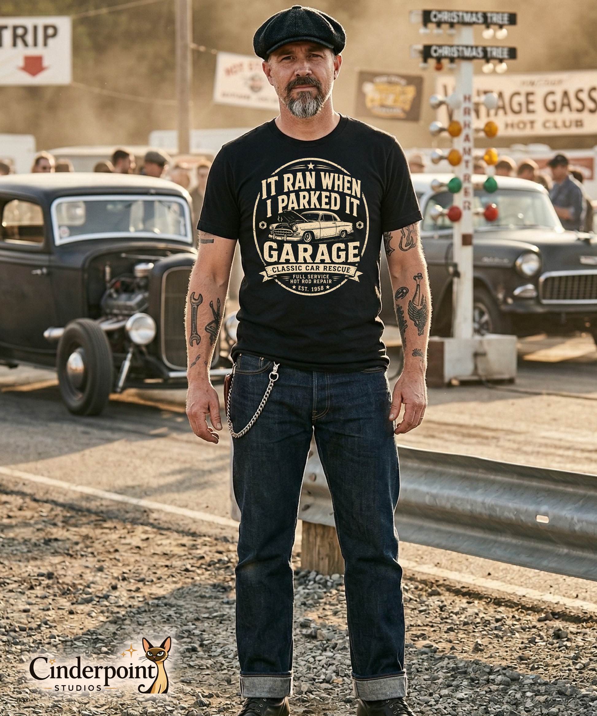 Man at drag strip wearing a black graphic tee featuring original Cinderpoint Studios artwork for It Ran When I Parked It Garage, a one-color funny classic car design with bold lettering, a vintage car with the hood up, Classic Car Rescue text, and Full Service Hot Rod Repair details.