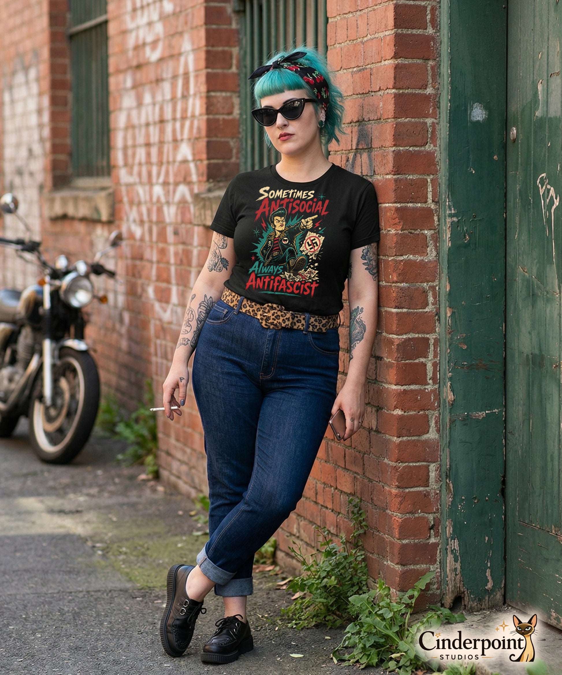 A gritty, lowbrow illustration on a black t-shirt of a pompadoured greaser in a leopard-print lined leather jacket, kicking over hate symbols. Text reads 'Sometimes Antisocial Always Antifascist' in a distressed punk-style font.