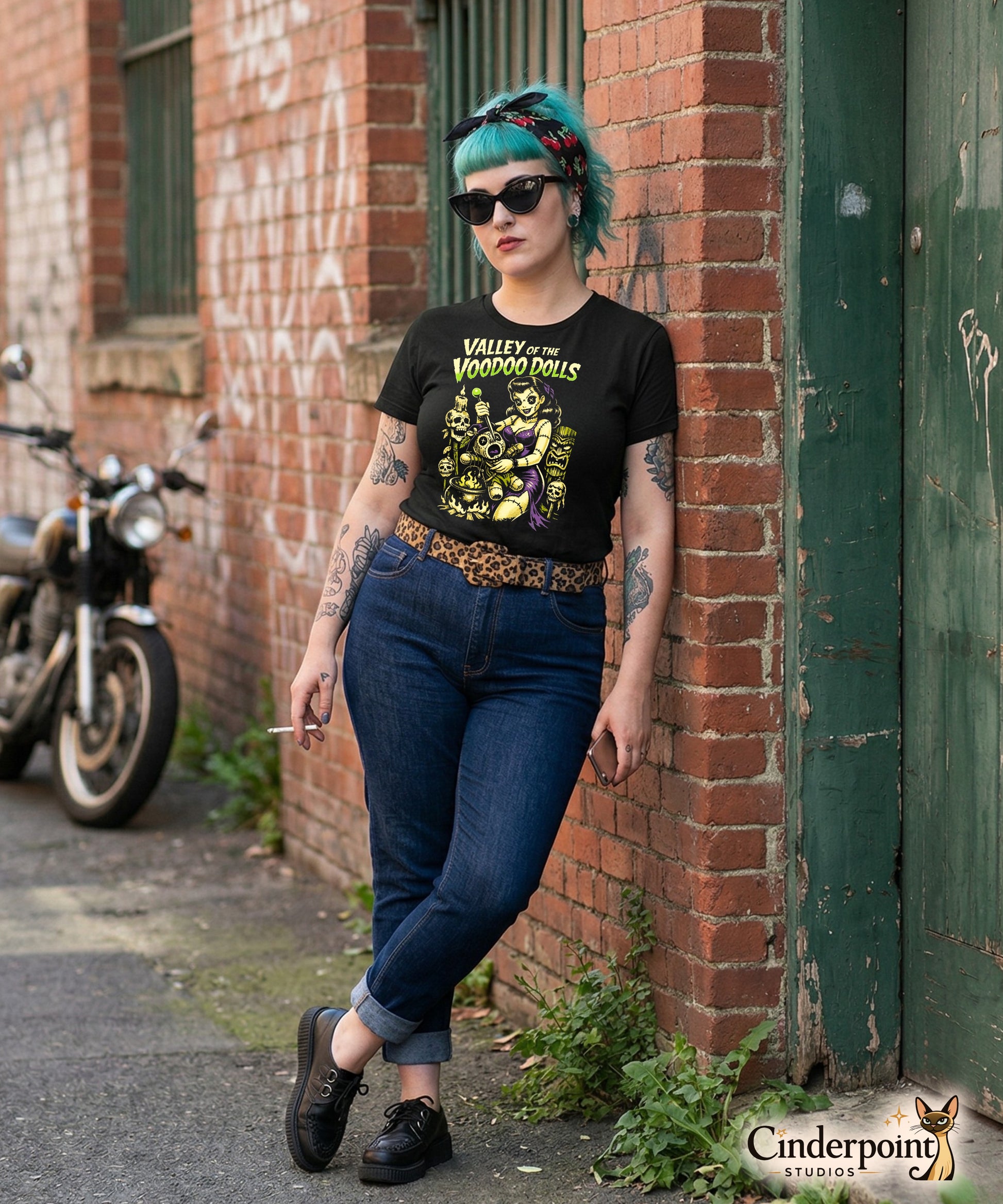 A retro-style graphic on a black t-shirt featuring a stylized pinup girl voodoo doll turning the tables on a medicine man in a vibrant, gritty Tiki-horror aesthetic