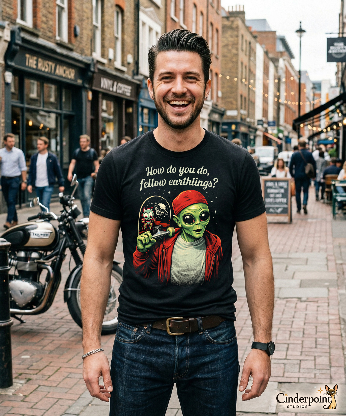 Happy man on the street wearing a retro-style graphic on a black t-shirt featuring a green alien on a skateboard, wearing a red hat and holding a skateboard, with the text "FELLOW EARTHLINGS.