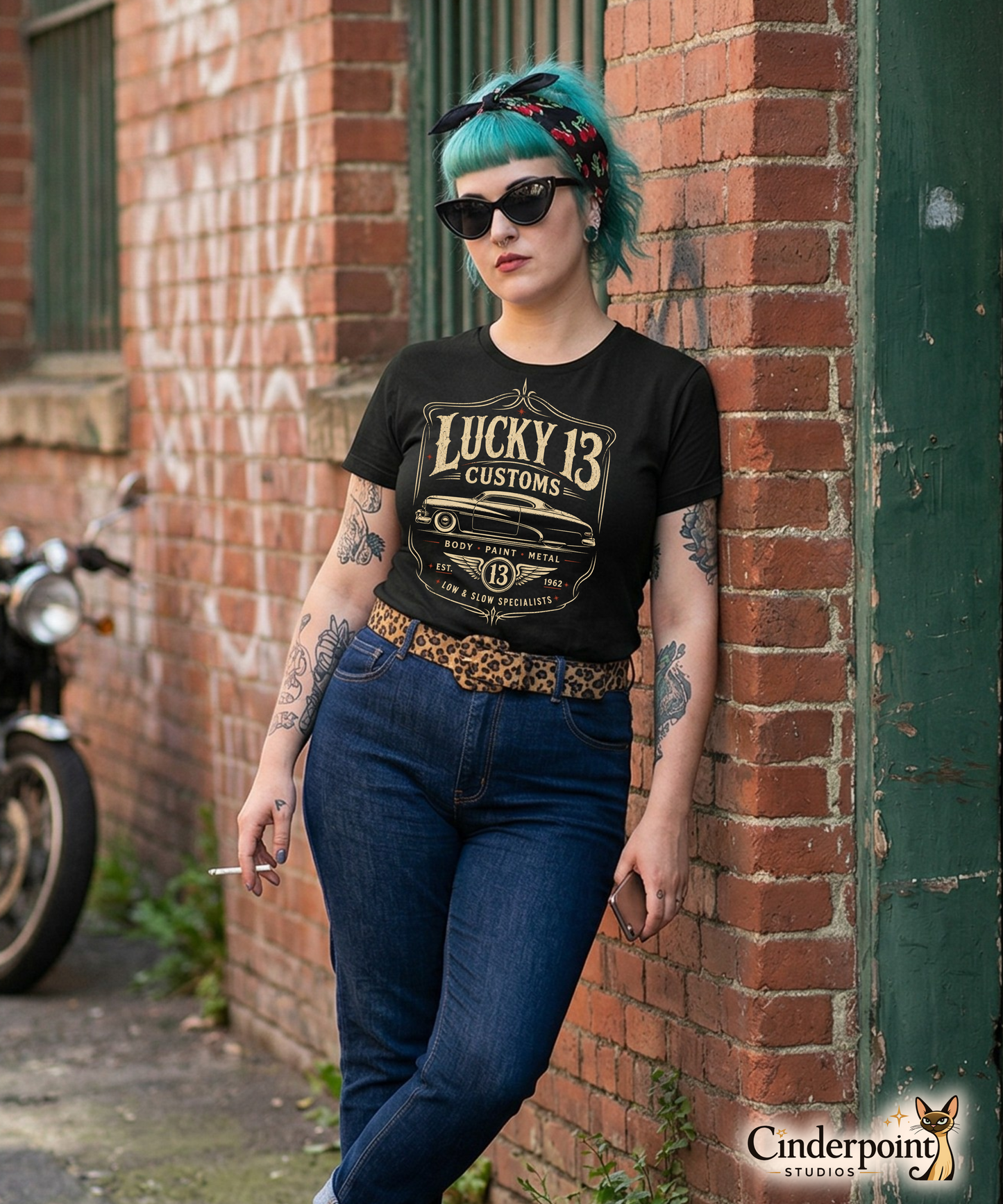 Punk rock girl leaning against a wall wearing a black graphic tee featuring original Cinderpoint Studios artwork for Lucky 13 Customs, a retro custom shop design with a lowrider-style classic car, bold vintage lettering, winged 13 emblem, pinstripe-style frame, and Low & Slow Specialists text.