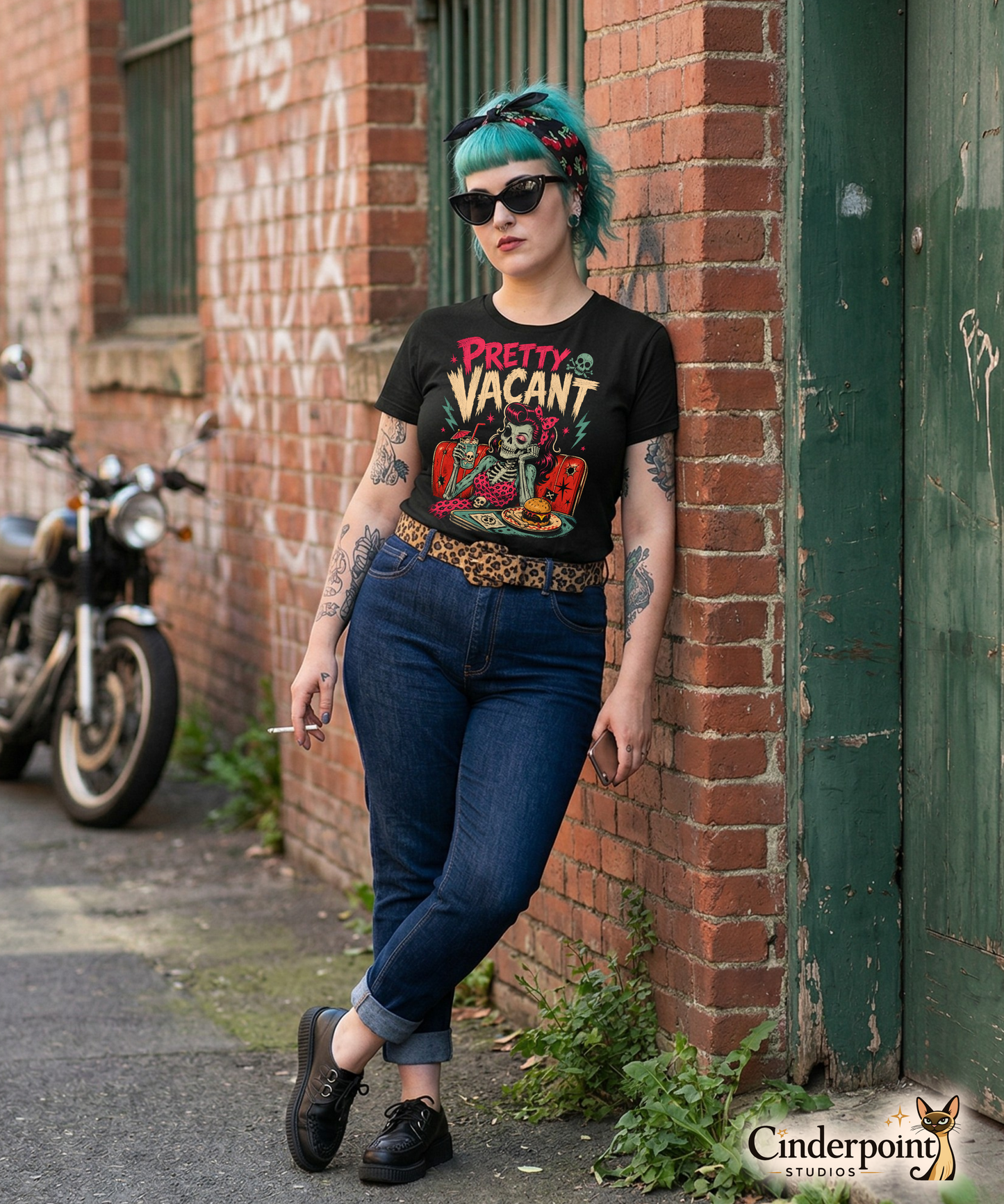 A retro-style graphic on a black t-shirt of a female skeleton pinup with pink hair in a diner booth, holding a skull-themed milkshake next to a burger with a crossbones flag.
