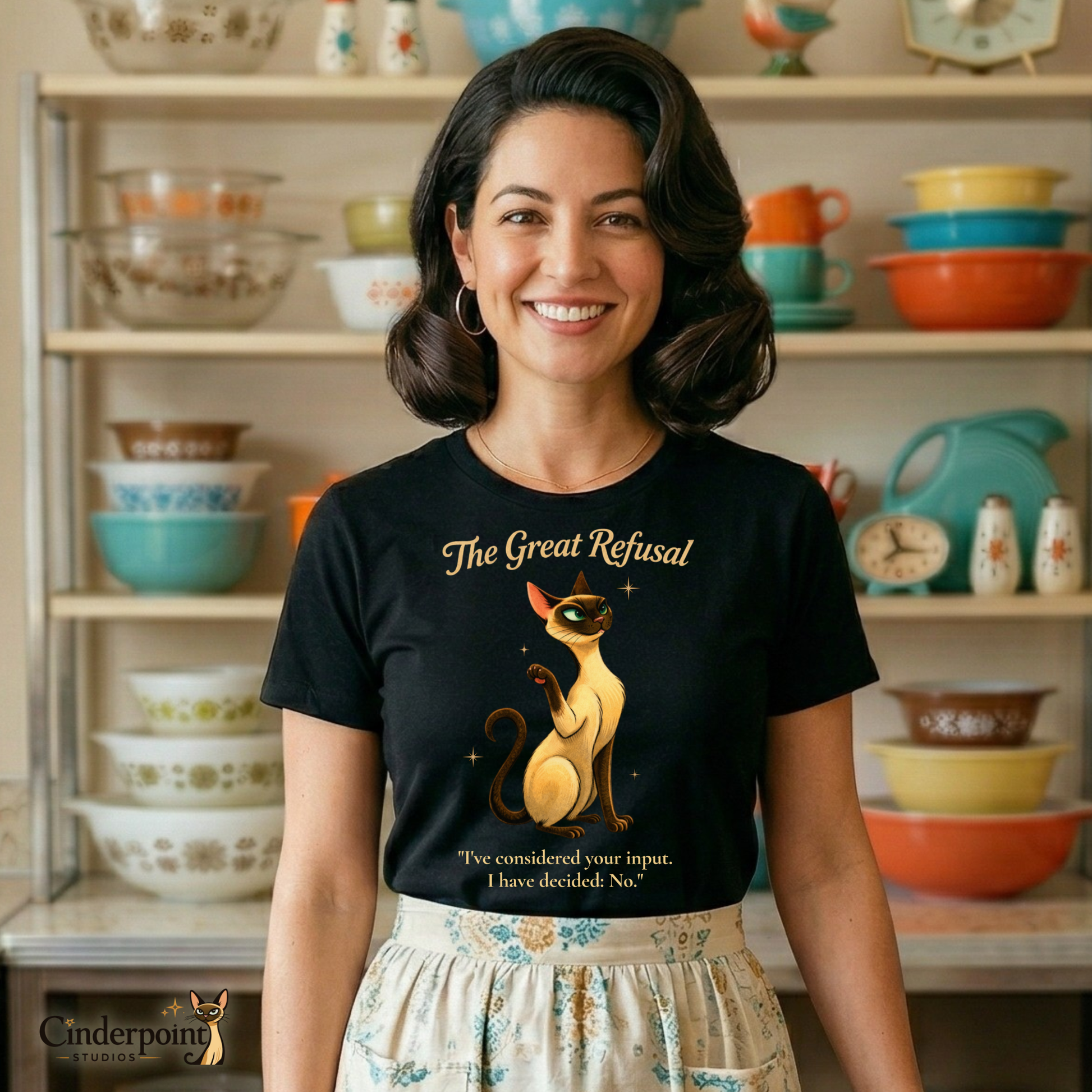A woman wearing a black t-shirt with a long-neck Siamese cat graphic and text, standing in front of a shelf with vintage kitchenware.