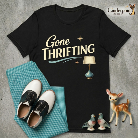 A black short-sleeved t-shirt featuring a 1950s style graphic. The words 'Gone THRIFTING' are in a bold, cream and gold script with a teal accent swirl and a detailed mid-century modern table lamp illustration.
