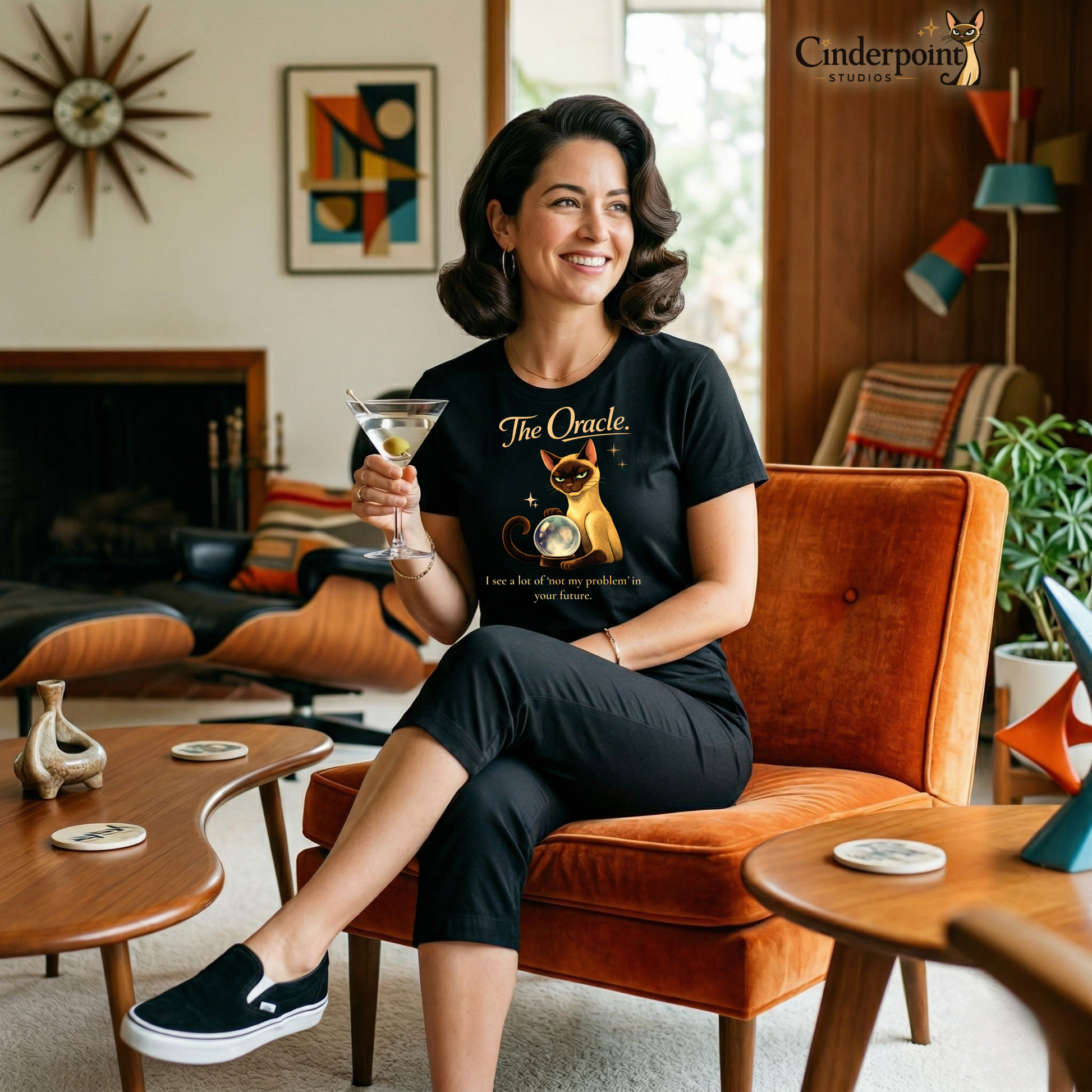 A woman with a vintage bob hairstyle wearing "The Oracle" Lyle the cat t-shirt, seated in a mid-century modern living room with a martini. She looks peaceful and detached, perfectly capturing the "Oracle" energy of the shirt.