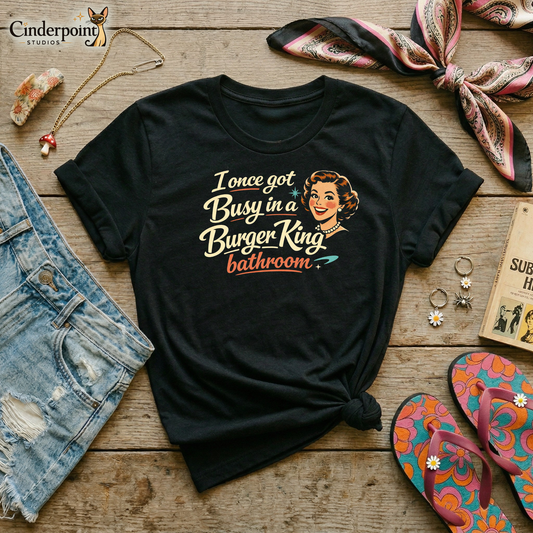 Flat layout of a black t-shirt with a 1950s housewife illustration that reads, "I once got busy in a Burger King Bathroom". Denim shorts, a retro hair scarf, psychedelic flip-flops, a mushroom necklace, daisy accents, and accessories surround the shirt. 