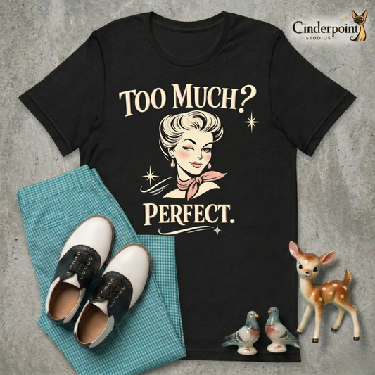A top-down flat-lay on a grey concrete surface featuring the 'Too Much? Perfect.' black tee. Included are teal gingham pants, black and white saddle shoes, and vintage ceramic figurines.