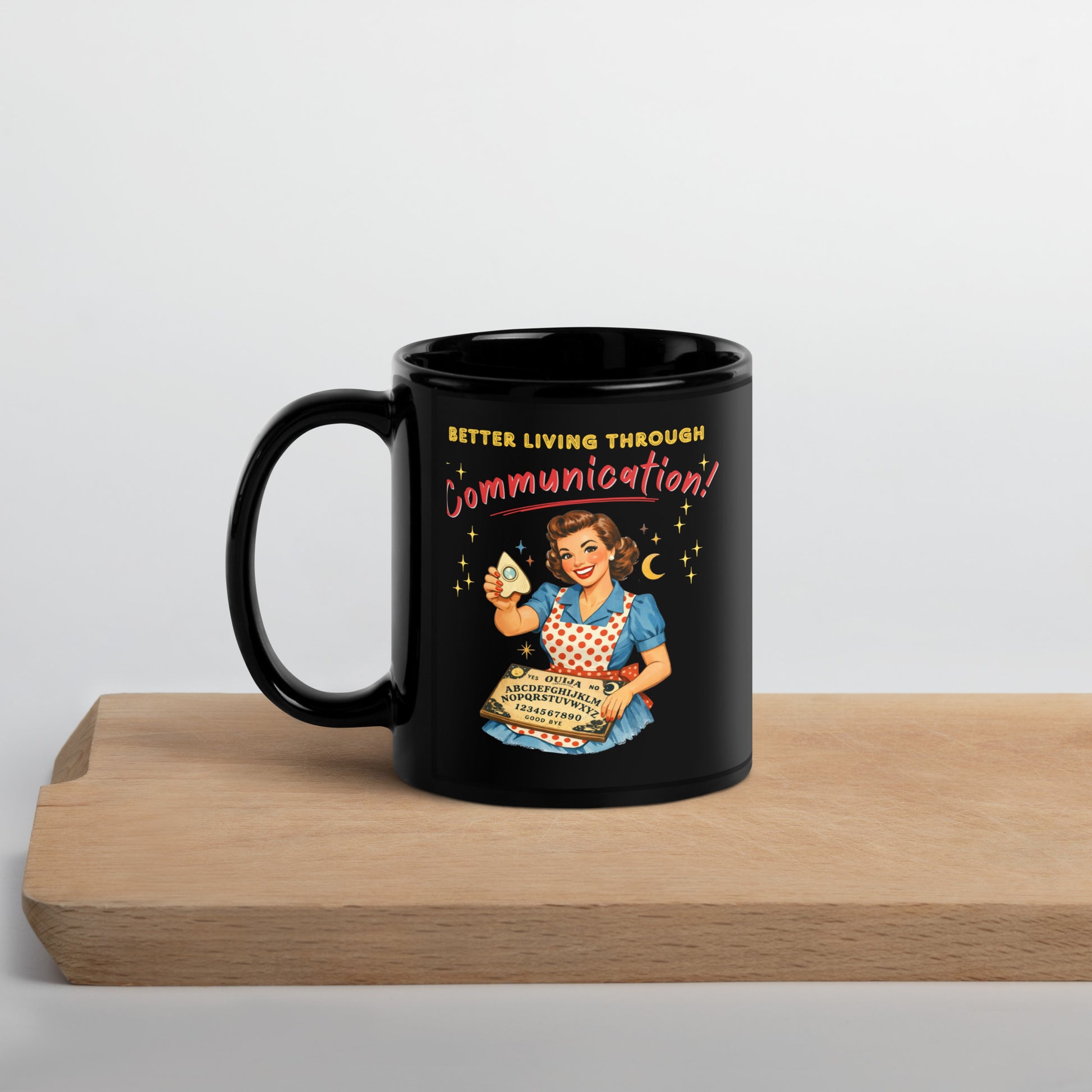 Better Living Through Communication black ceramic mug — vintage 1950s retro housewife in polka dot apron holding ouija board and planchette, printed on both sides by Cinderpoint Studios