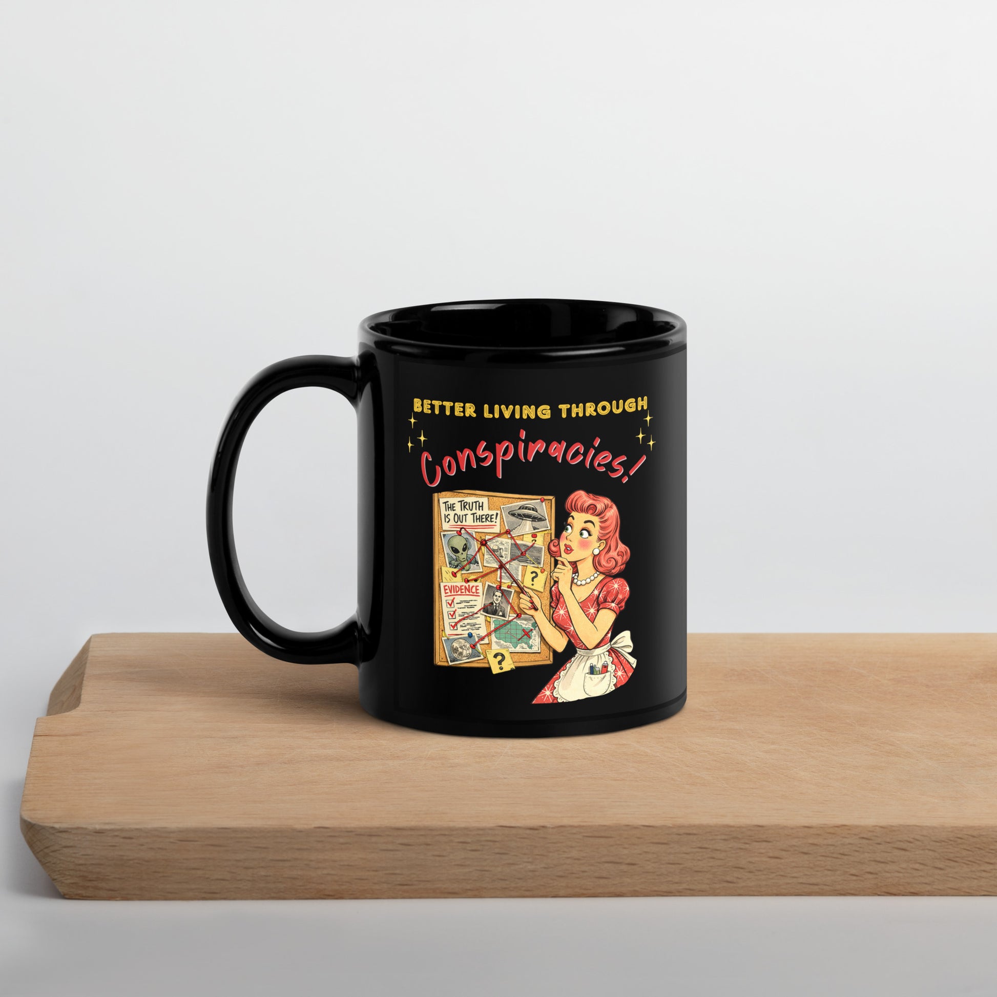 Better Living Through Conspiracies black ceramic mug — vintage 1950s retro housewife pointing at alien evidence cork board with red string and UFO photos, printed on both sides by Cinderpoint Studios