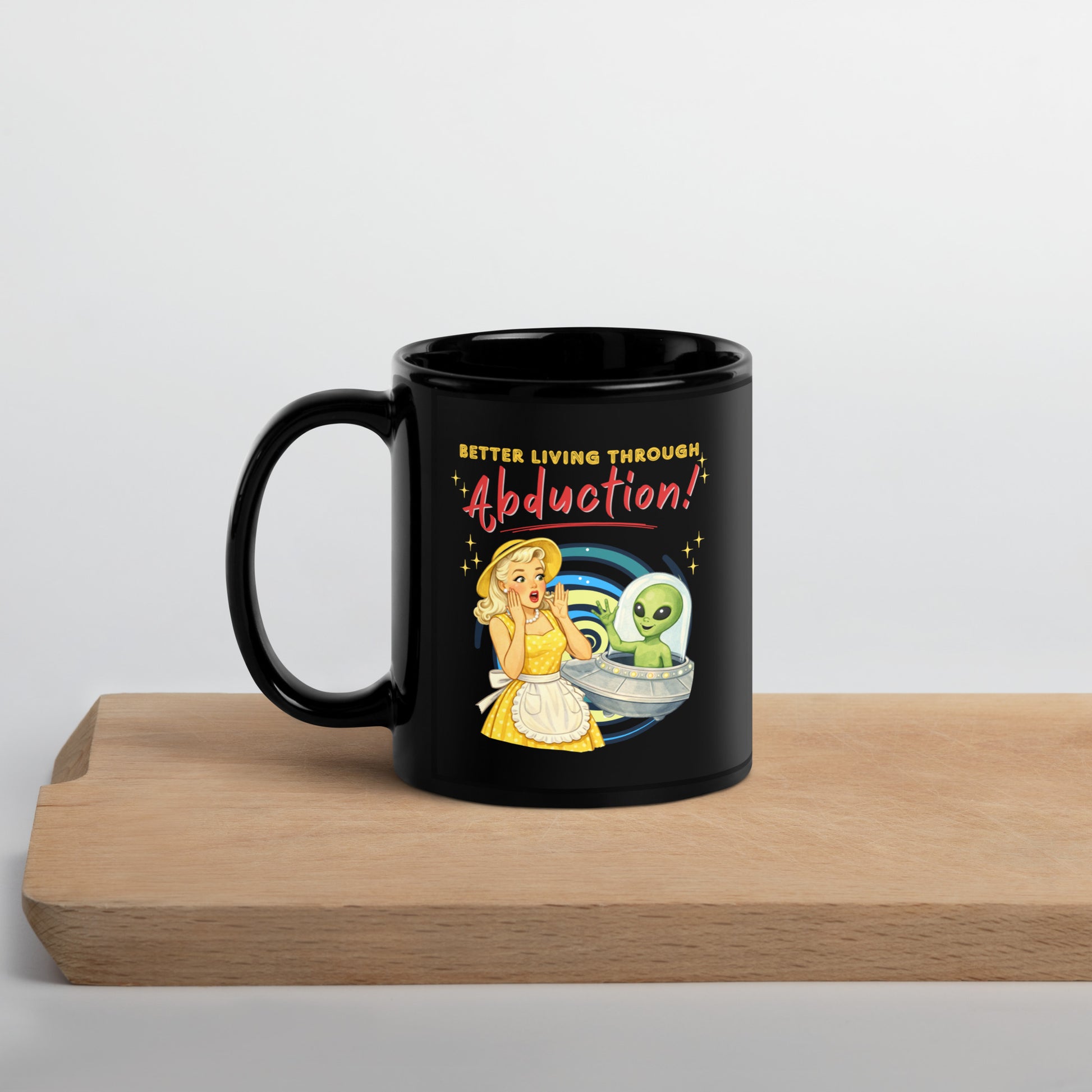 Better Living Through Abduction black ceramic mug — vintage 1950s retro blonde housewife in yellow polka dot dress reacting with delight to a friendly green alien waving from a silver saucer, printed on both sides by Cinderpoint Studios