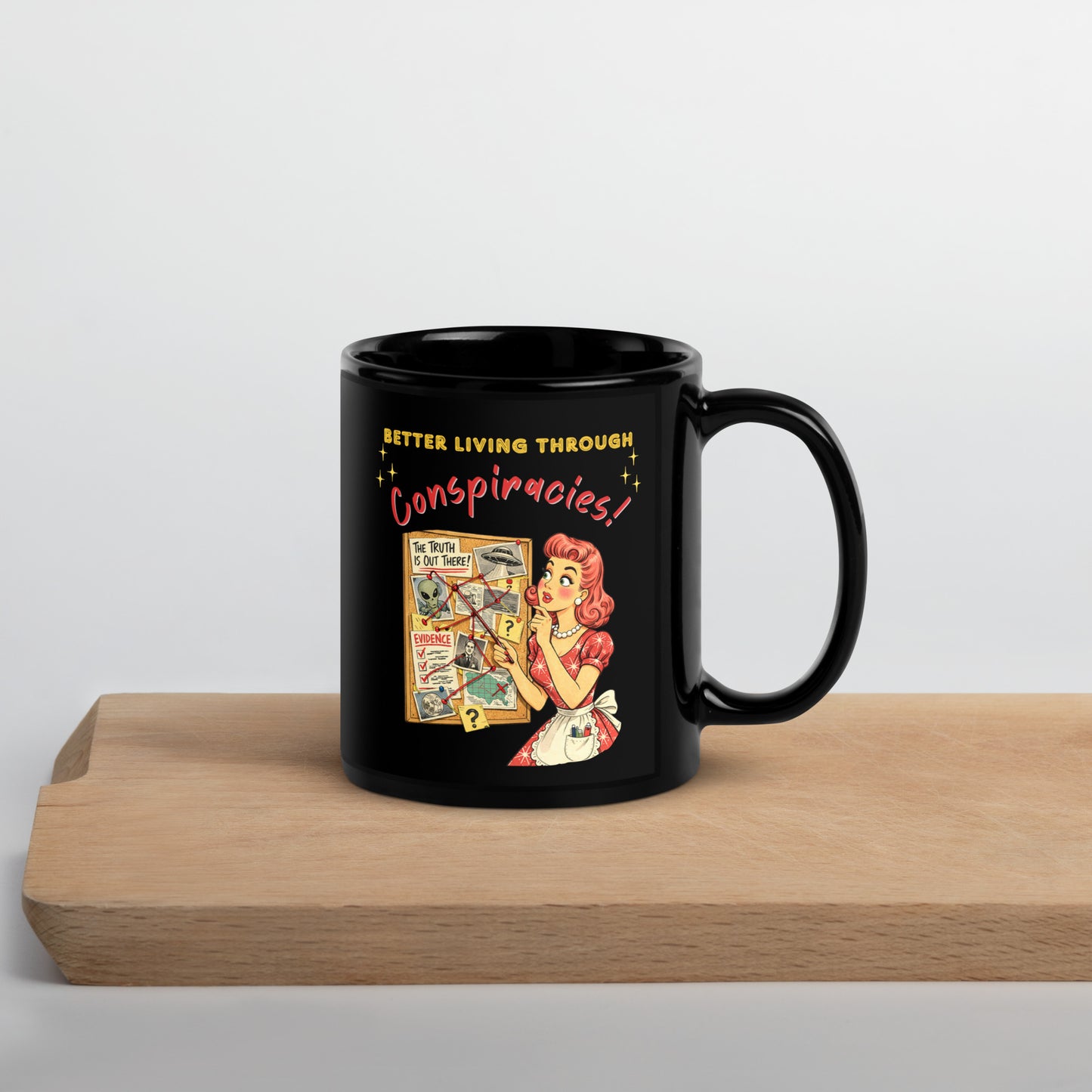 Better Living Through Conspiracies black ceramic mug — vintage 1950s retro housewife pointing at alien evidence cork board with red string and UFO photos, printed on both sides by Cinderpoint Studios