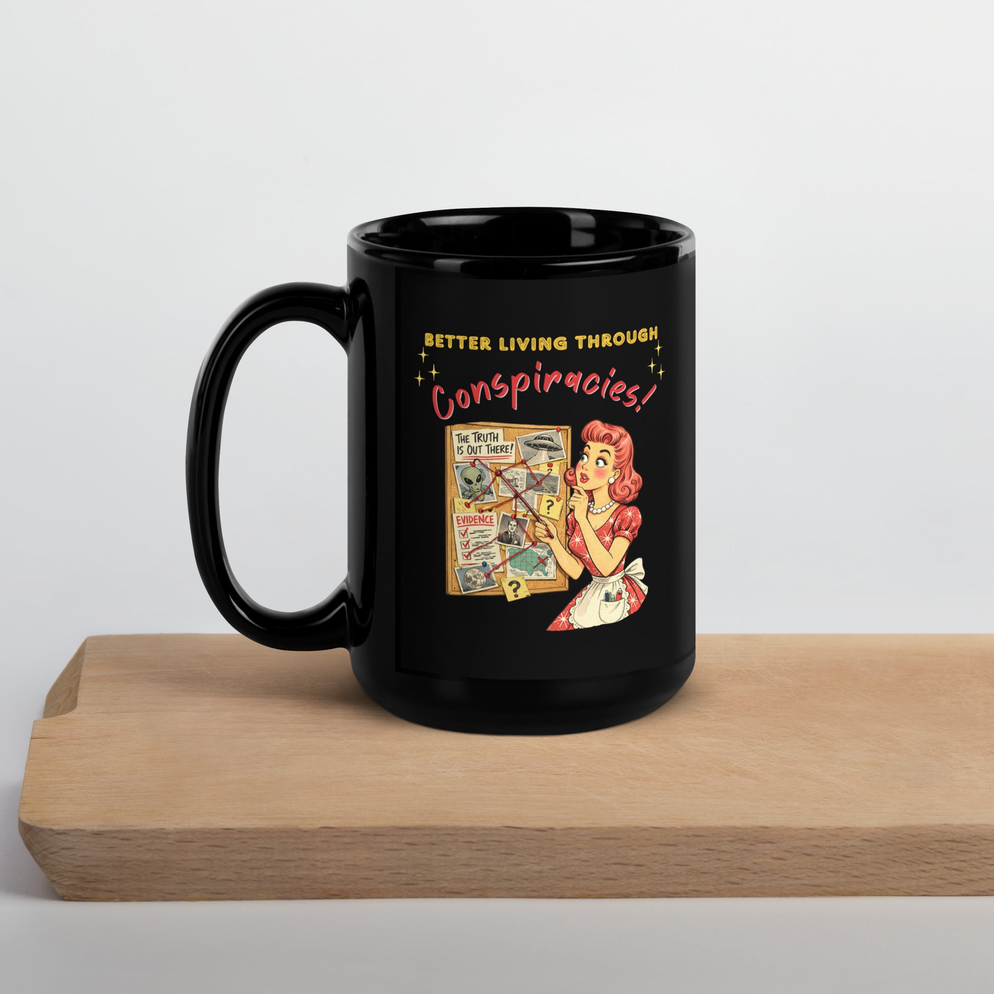 Better Living Through Conspiracies black ceramic mug — vintage 1950s retro housewife pointing at alien evidence cork board with red string and UFO photos, printed on both sides by Cinderpoint Studios