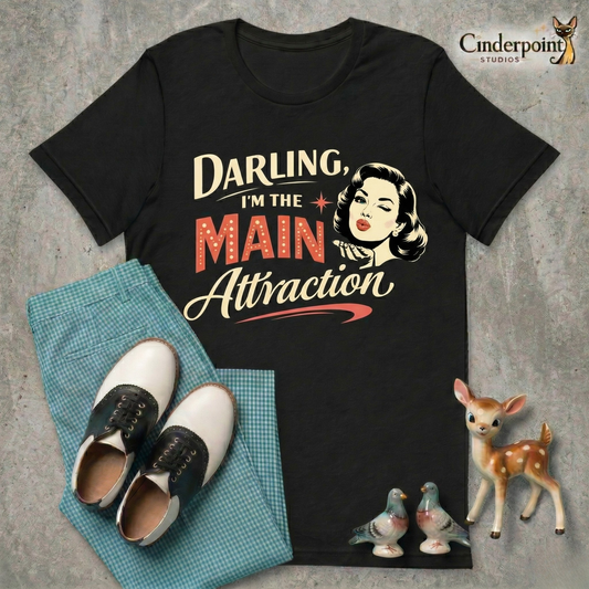 A top-down flat-lay on a grey concrete surface featuring the 'Main Attraction' black tee. Included are teal gingham pants, black and white saddle shoes, and vintage ceramic figurines.