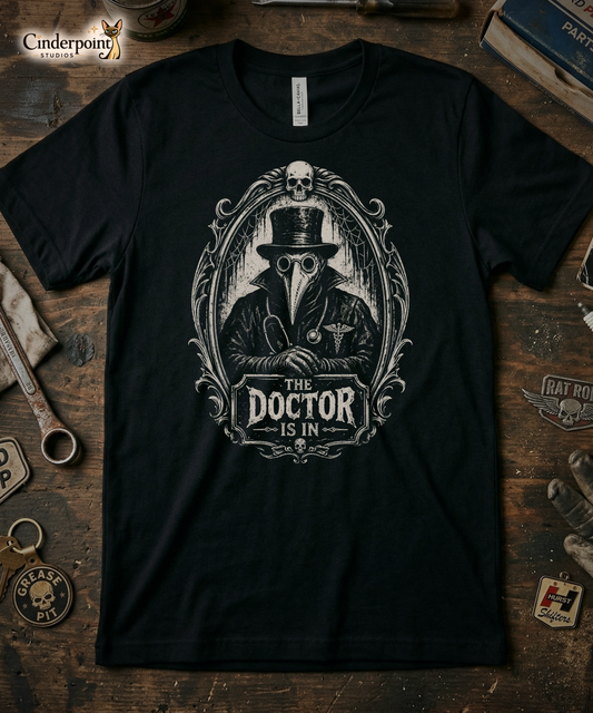 Top-down flat lay of a black Bella Canvas 3001 t-shirt with the Victorian 'The Doctor Is In' plague doctor design on a rustic wooden workshop table with a wrench, spark plug, and vintage car club patches.