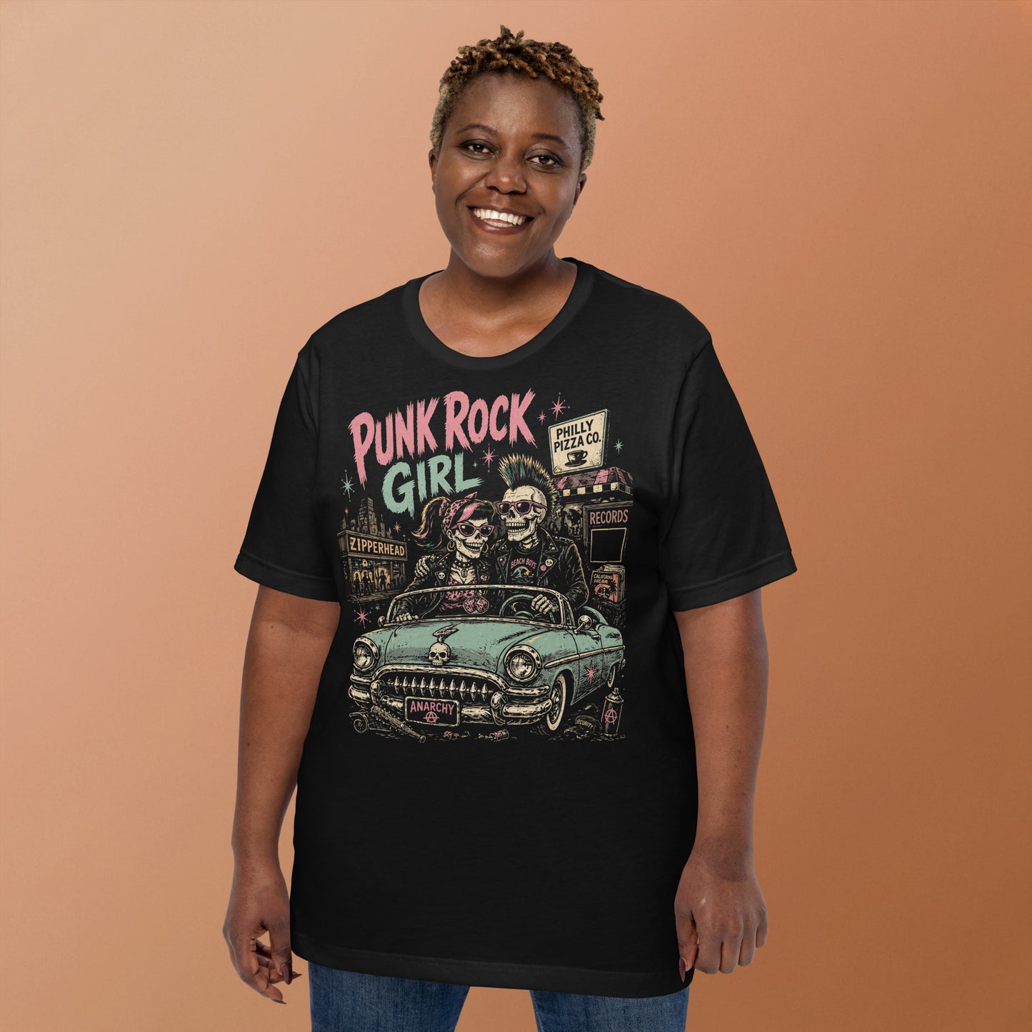 A retro-style graphic on a black t-shirt featuring two skeletons—a male with a mohawk and a female with a pink bow—driving a teal 1955 Chevy past iconic Philadelphia punk landmarks.