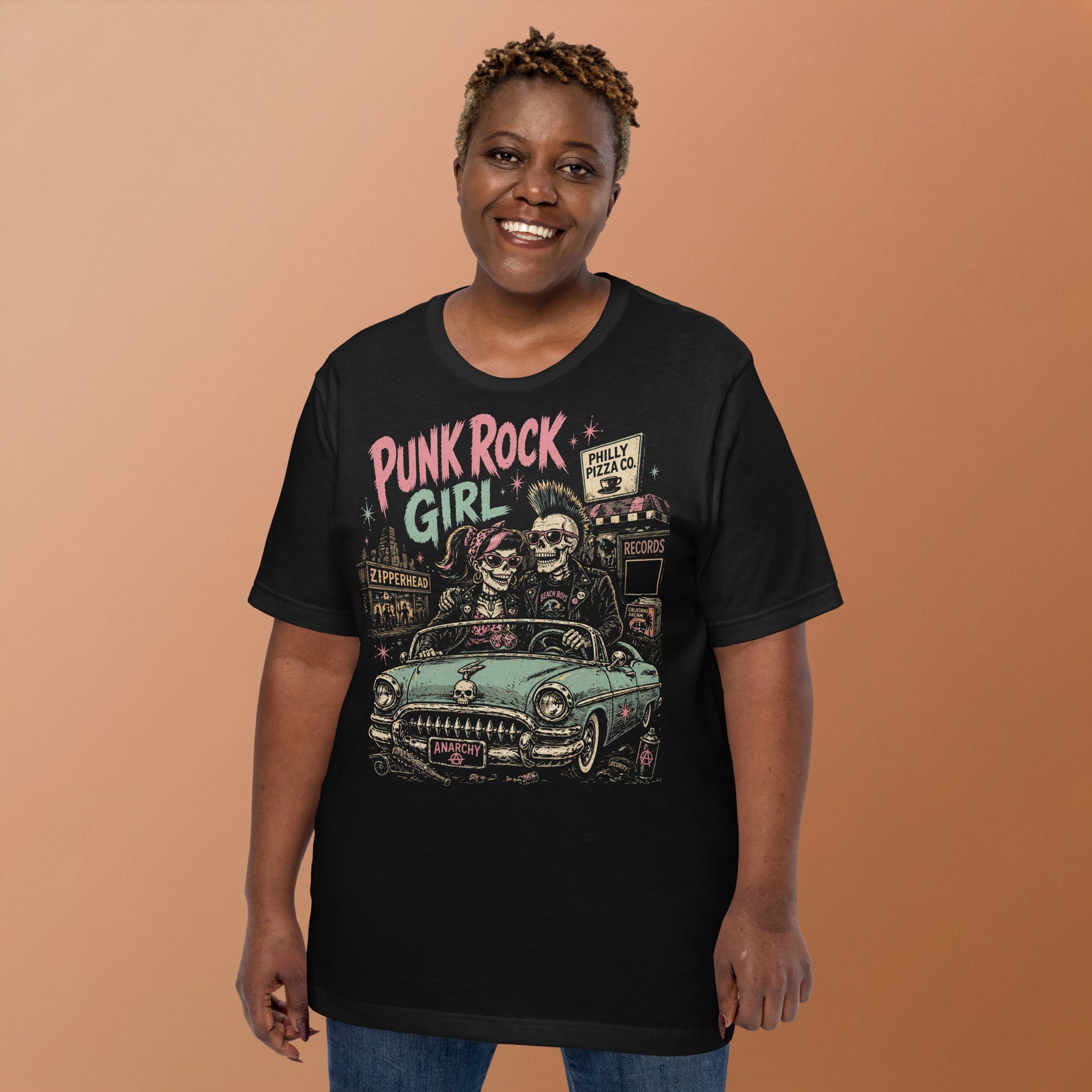 A retro-style graphic on a black t-shirt featuring two skeletons—a male with a mohawk and a female with a pink bow—driving a teal 1955 Chevy past iconic Philadelphia punk landmarks.