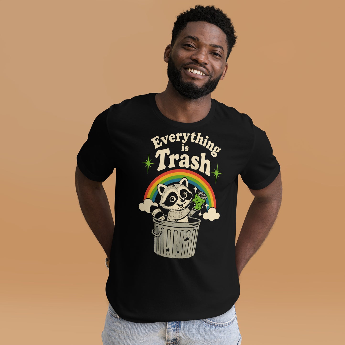 A retro 1970s-style graphic t-shirt featuring a cute raccoon sitting under a vibrant rainbow with the text "Everything Is Trash" in vintage-inspired lettering