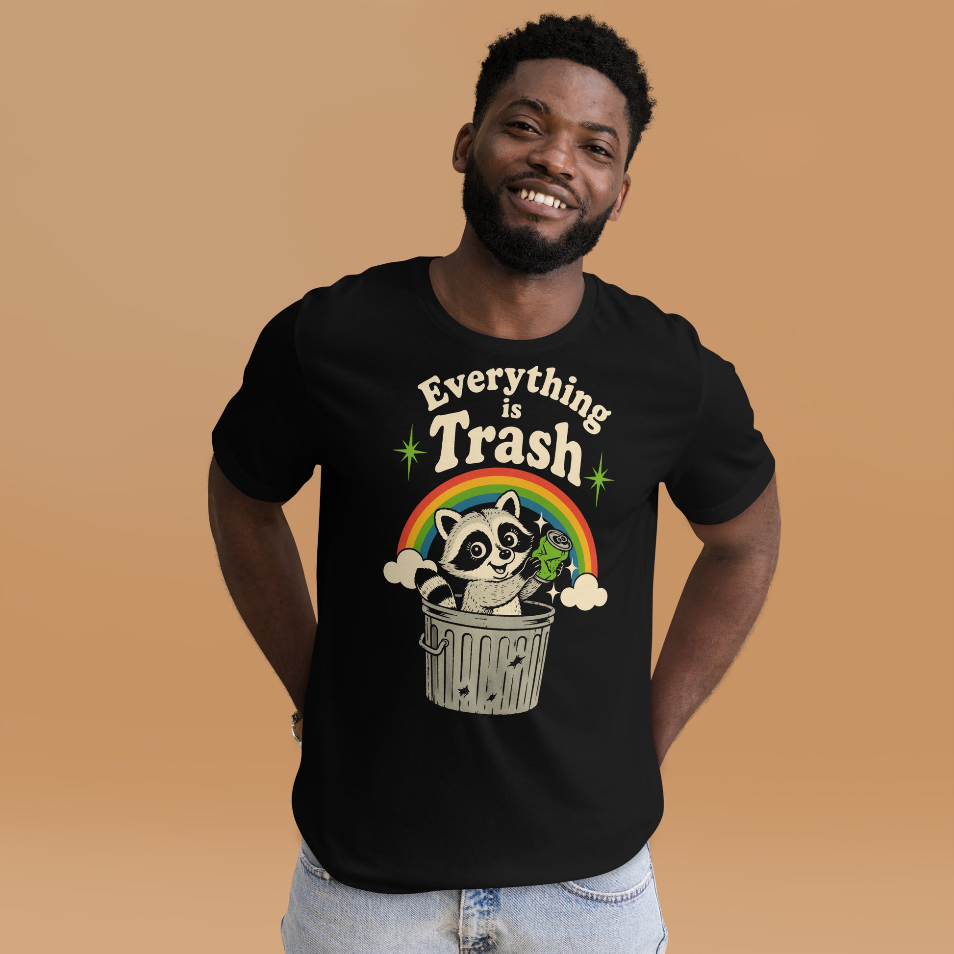 A retro 1970s-style graphic t-shirt featuring a cute raccoon sitting under a vibrant rainbow with the text "Everything Is Trash" in vintage-inspired lettering