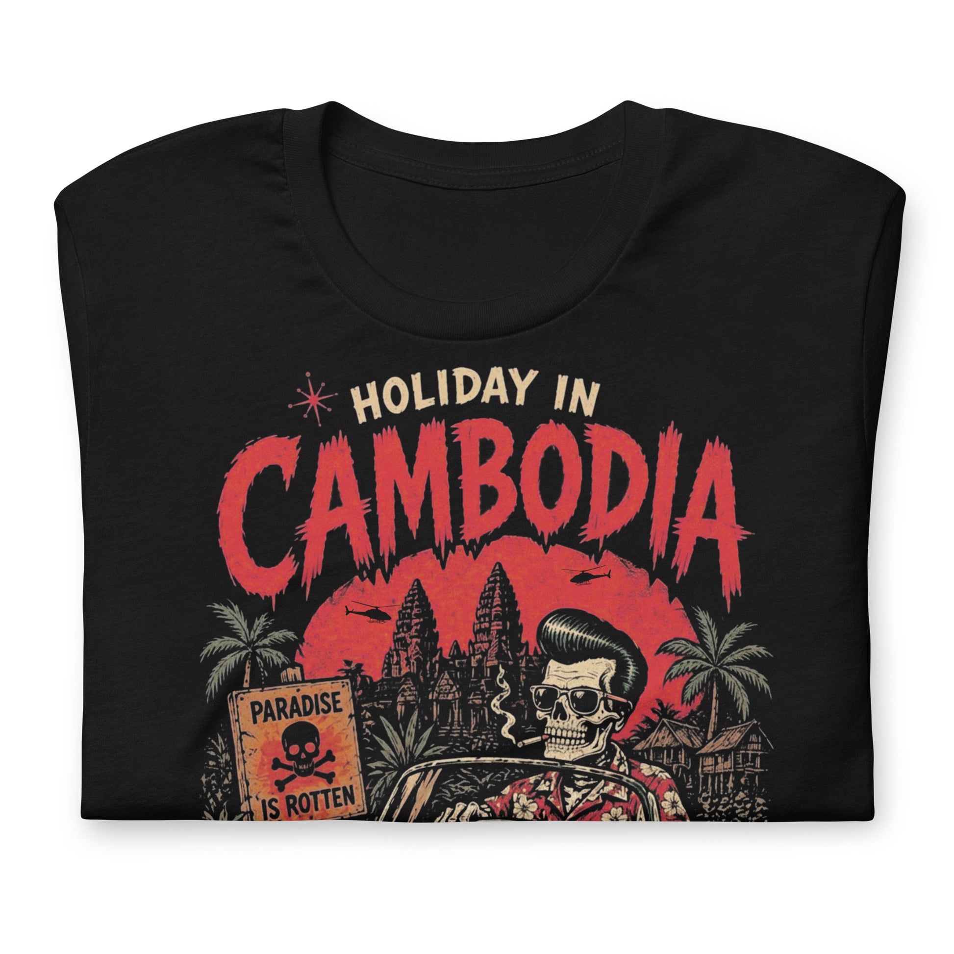 A detailed lowbrow graphic on a black t-shirt featuring a skeleton with a pompadour driving a 1955 Chevy convertible. The background shows Angkor Wat under a red sun with helicopters, and a sign that reads 'Paradise is Rotten'.