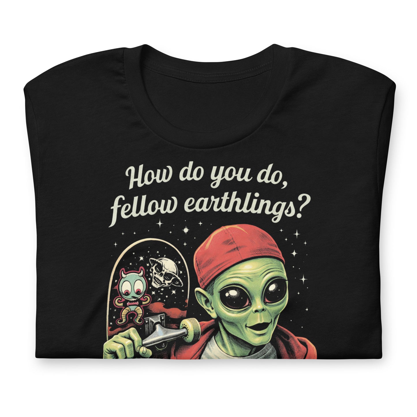 A retro-style graphic on a black t-shirt featuring a green alien on a skateboard, wearing a red hat and holding a skateboard, with the text "FELLOW EARTHLINGS.