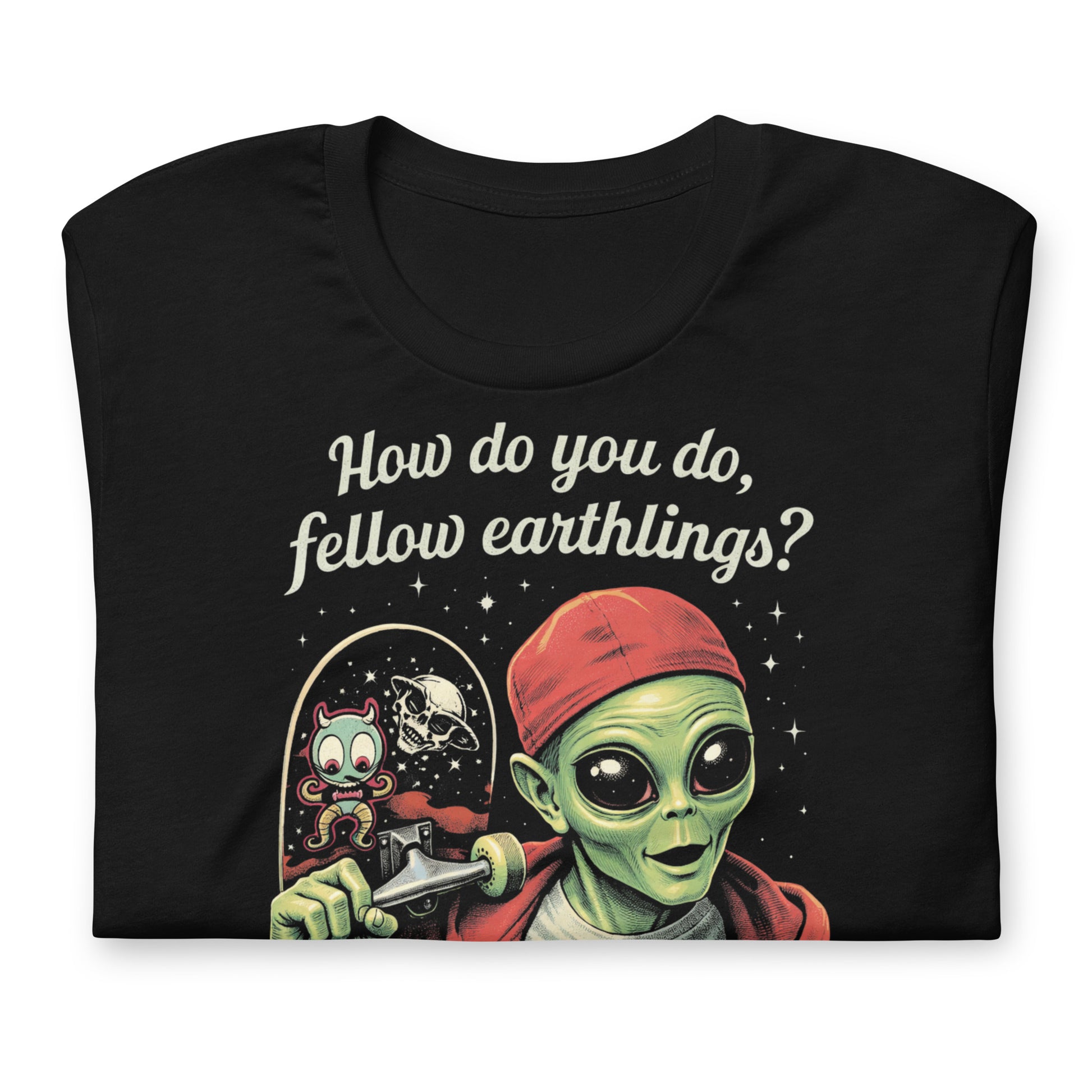 A retro-style graphic on a black t-shirt featuring a green alien on a skateboard, wearing a red hat and holding a skateboard, with the text "FELLOW EARTHLINGS.