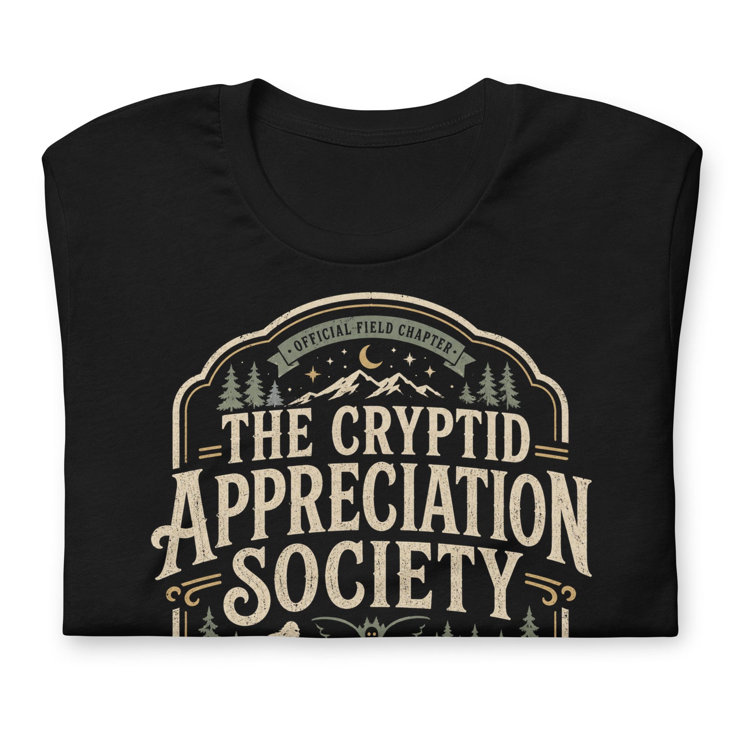 Black graphic tee featuring original Cinderpoint Studios artwork for The Cryptid Appreciation Society, a retro cryptid badge design with Sasquatch, Mothman, a Nessie-style lake creature, forest, mountains, moon, stars, and We Believe text.