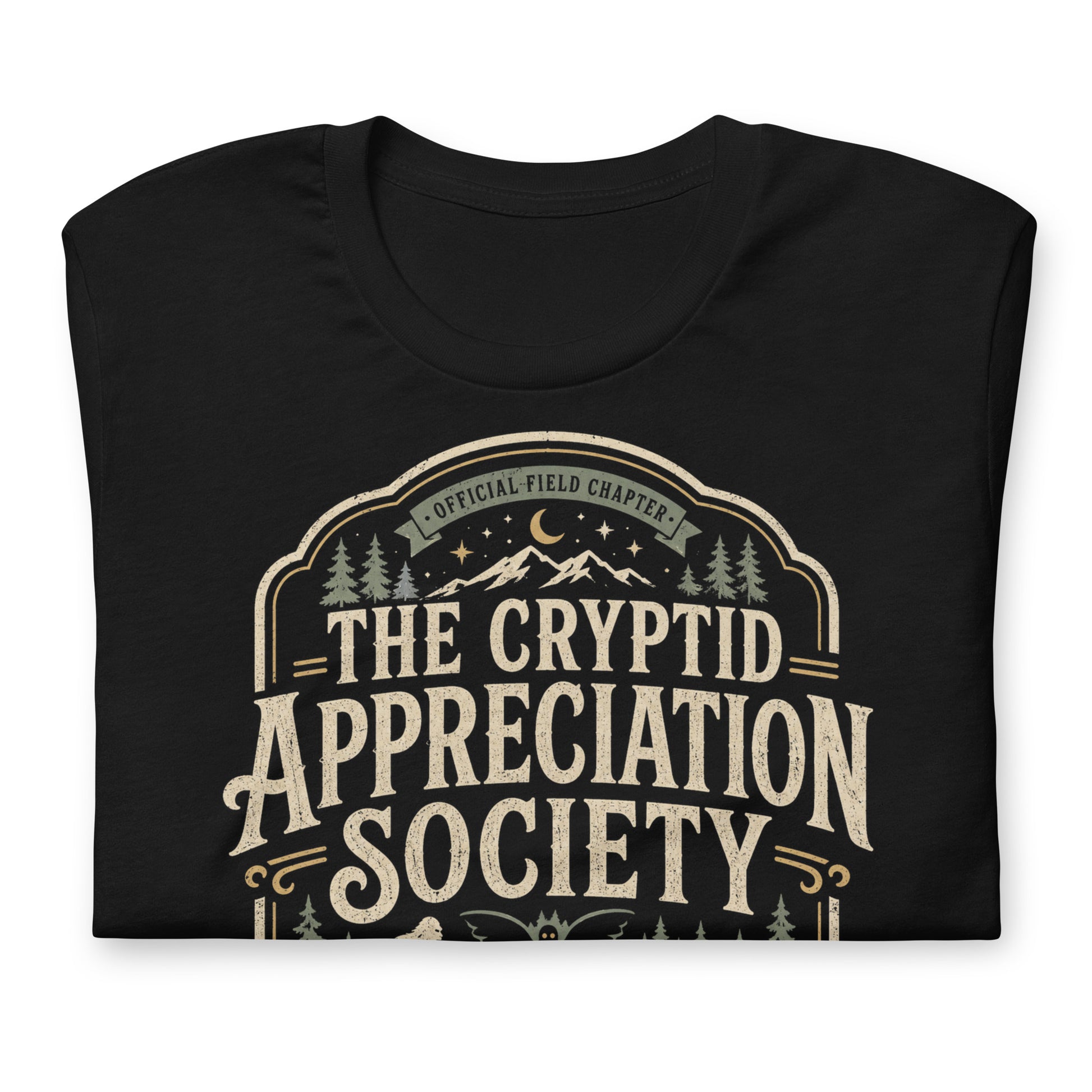 Black graphic tee featuring original Cinderpoint Studios artwork for The Cryptid Appreciation Society, a retro cryptid badge design with Sasquatch, Mothman, a Nessie-style lake creature, forest, mountains, moon, stars, and We Believe text.