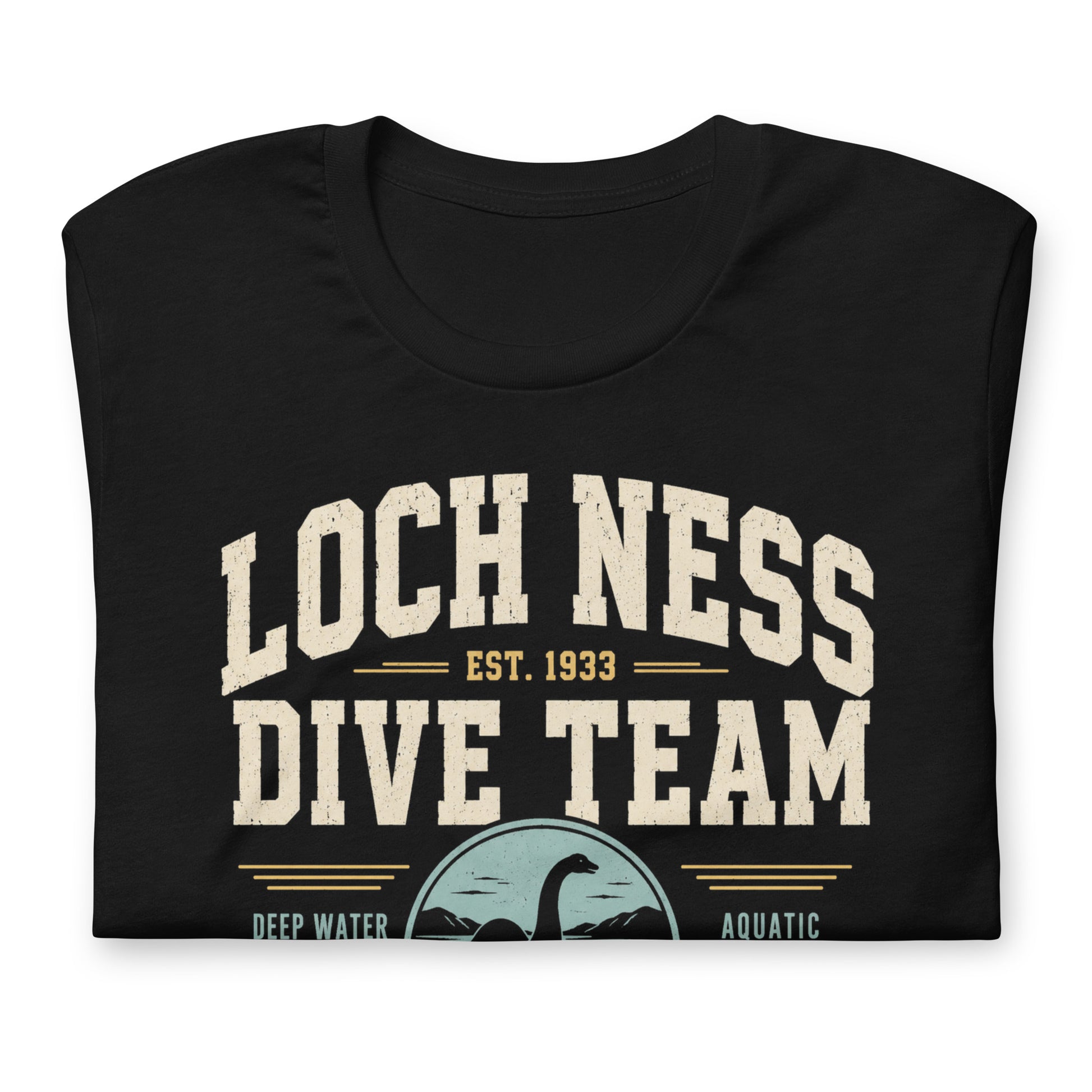 Black graphic tee featuring original Cinderpoint Studios artwork for Loch Ness Dive Team, a retro cryptid design with bold varsity lettering, a Nessie-style lake monster, diver, water scene, and text including Deep Water Division, Aquatic Observation Unit, We Believe, and Scotland Chapter.