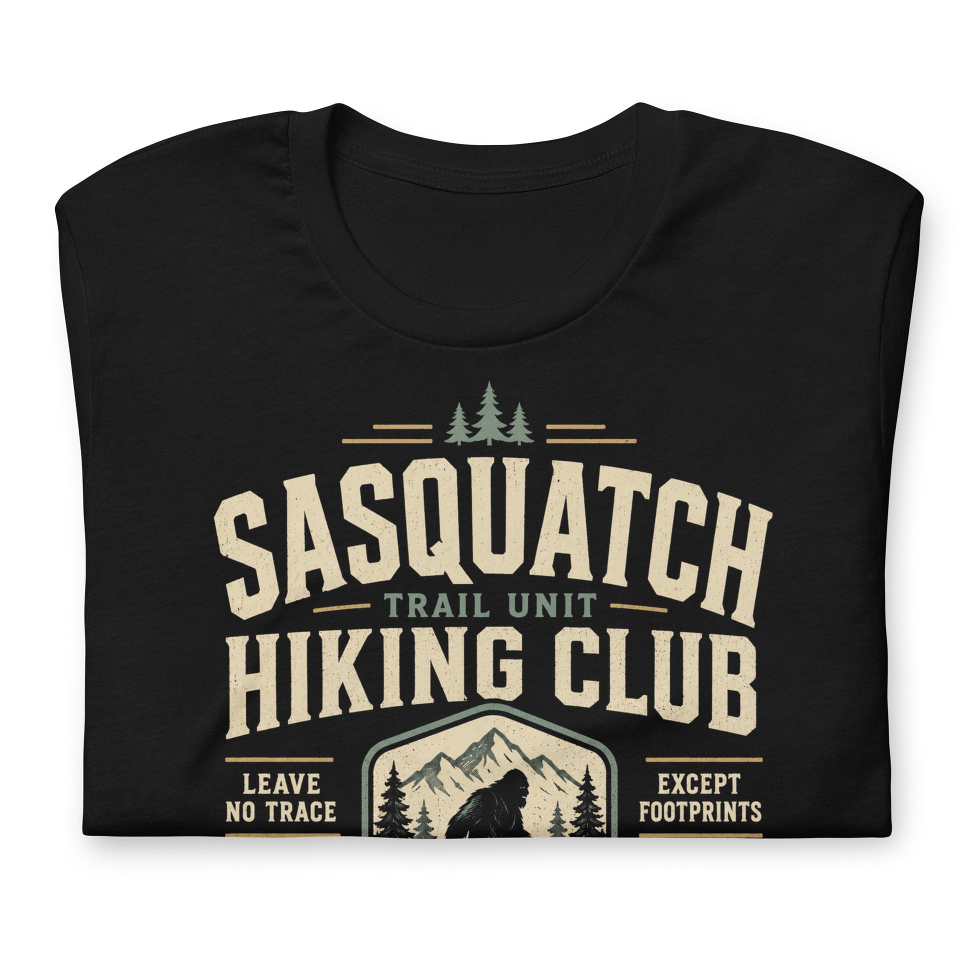 Close-up of the Sasquatch Hiking Club original Cinderpoint Studios artwork printed on a black tee, showing distressed retro lettering, Sasquatch silhouette, mountain scenery, pine trees, footprints, and Official Forest Division details.