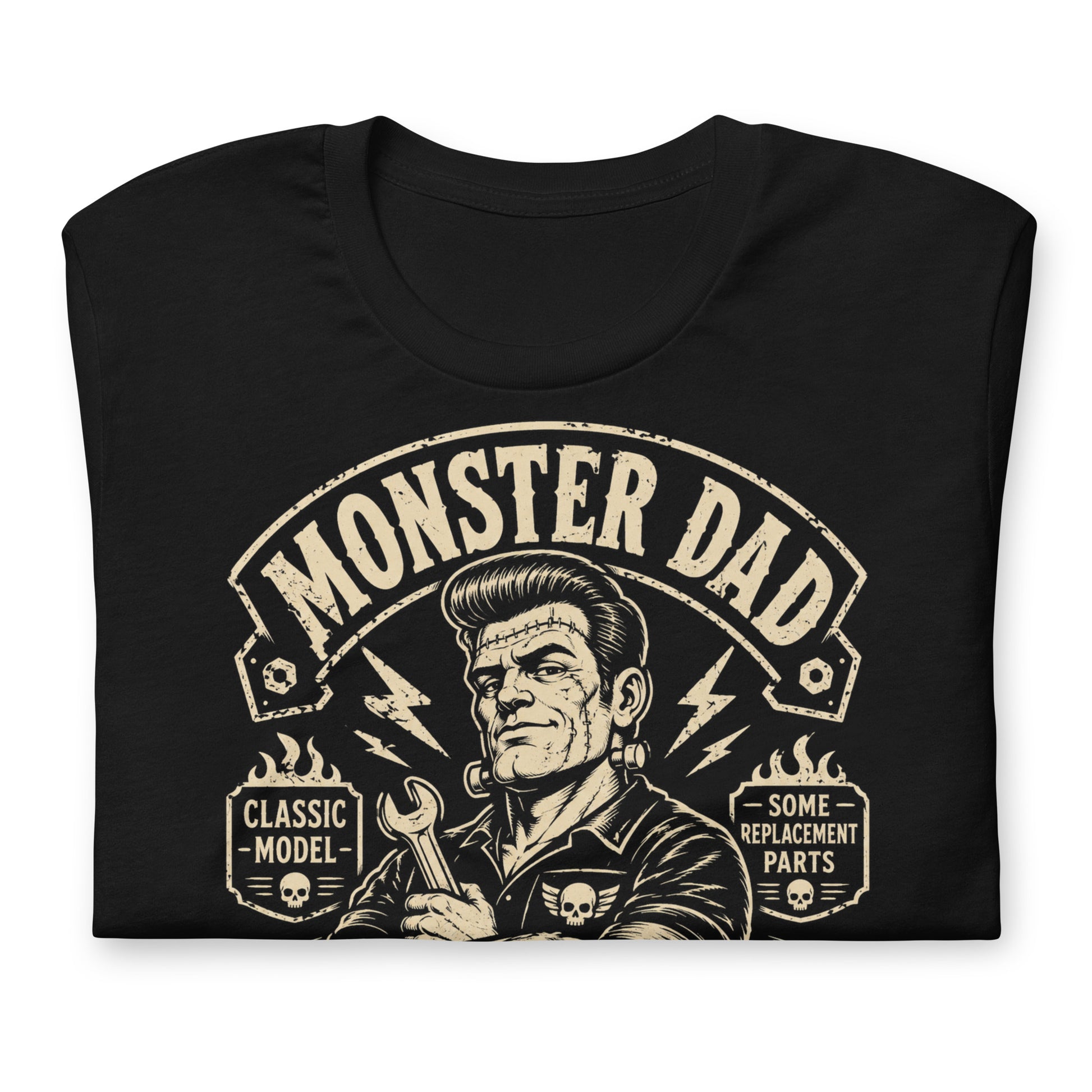 A black graphic tee featuring original Cinderpoint Studios artwork for Monster Dad Motor Club, a one-color retro garage design with a Frankenstein-inspired dad mechanic holding a wrench, lightning bolts, flames, skull details, piston accents, and text including Classic Model and Some Replacement Parts.