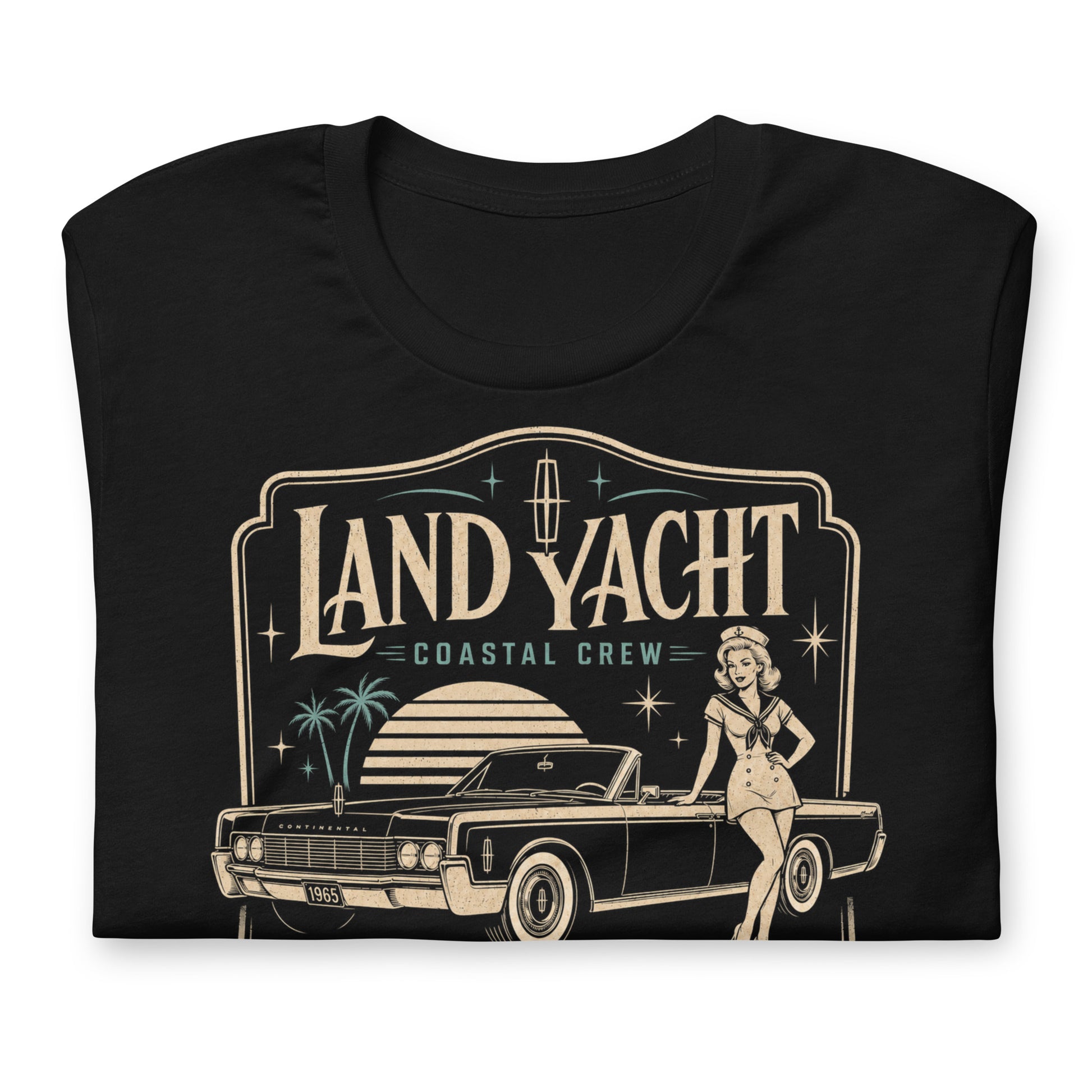 A black graphic tee featuring original Cinderpoint Studios artwork for Land Yacht Luxury Cruisers, a retro classic car design with a 1960s luxury convertible inspired by the 1965 Continental, a sailor pinup, atomic accents, palm trees, and bold vintage lettering.