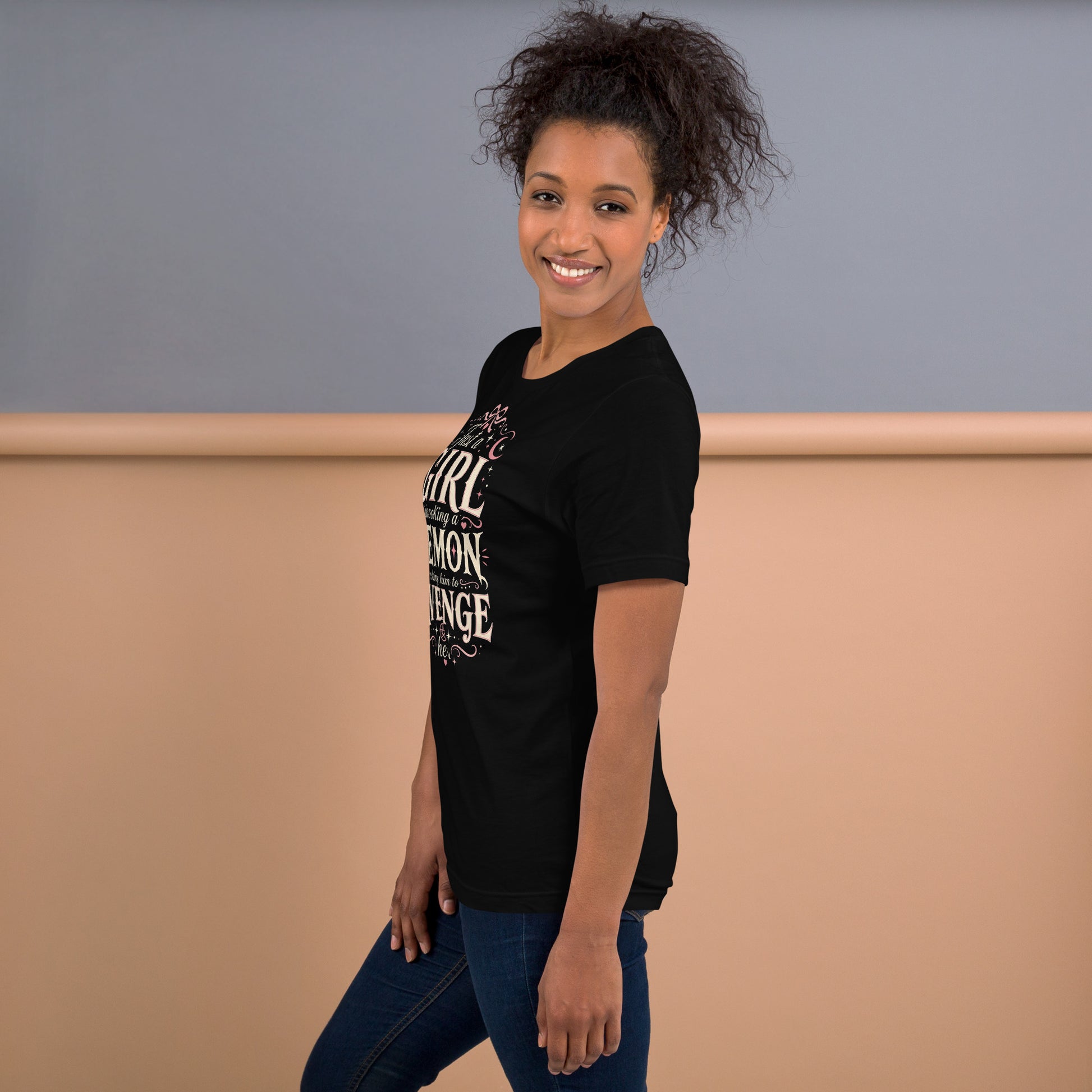 A pretty woman wearing a black graphic tee featuring original Cinderpoint Studios artwork for Just a Girl Invoking a Demon, a feminine occult humor design with bold vintage lettering, pink bow accents, crescent moon, stars, hearts, and a small pentagram.