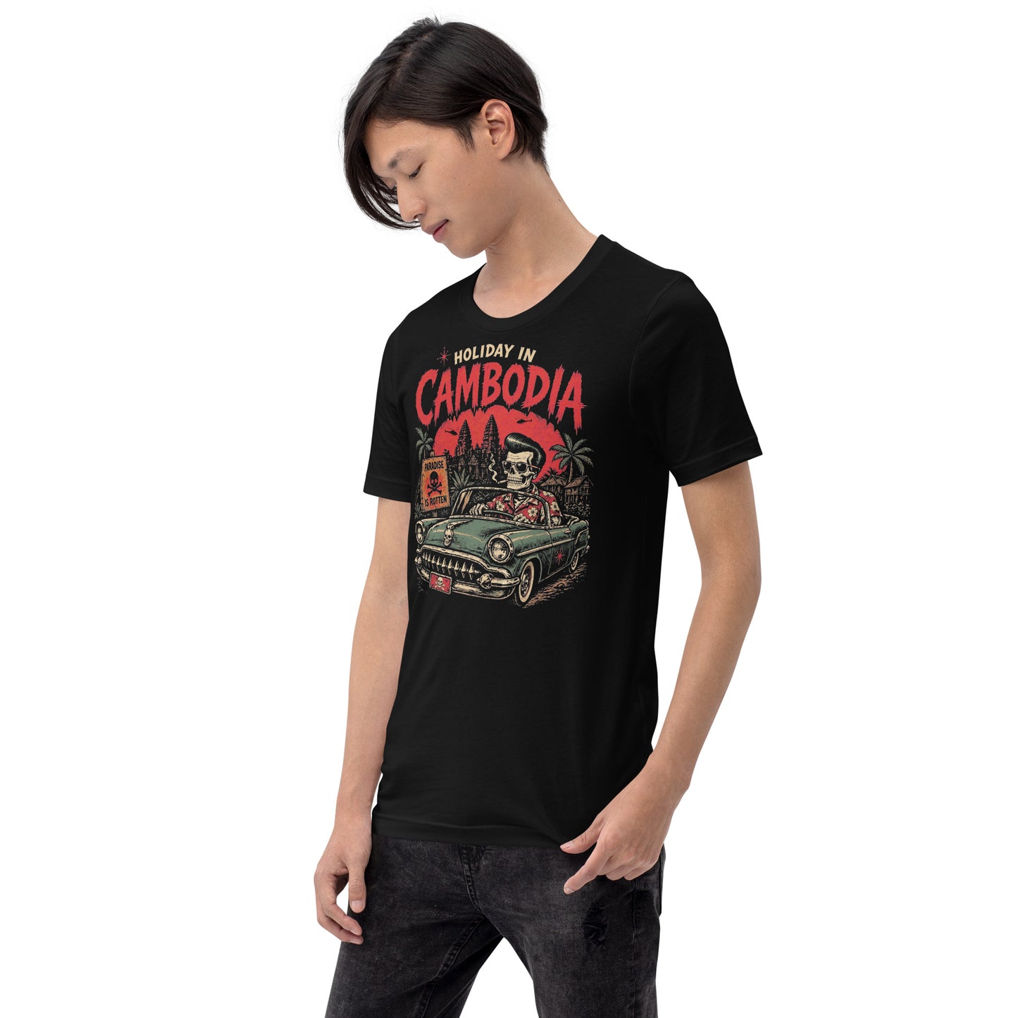 A detailed lowbrow graphic on a black t-shirt featuring a skeleton with a pompadour driving a 1955 Chevy convertible. The background shows Angkor Wat under a red sun with helicopters, and a sign that reads 'Paradise is Rotten'.