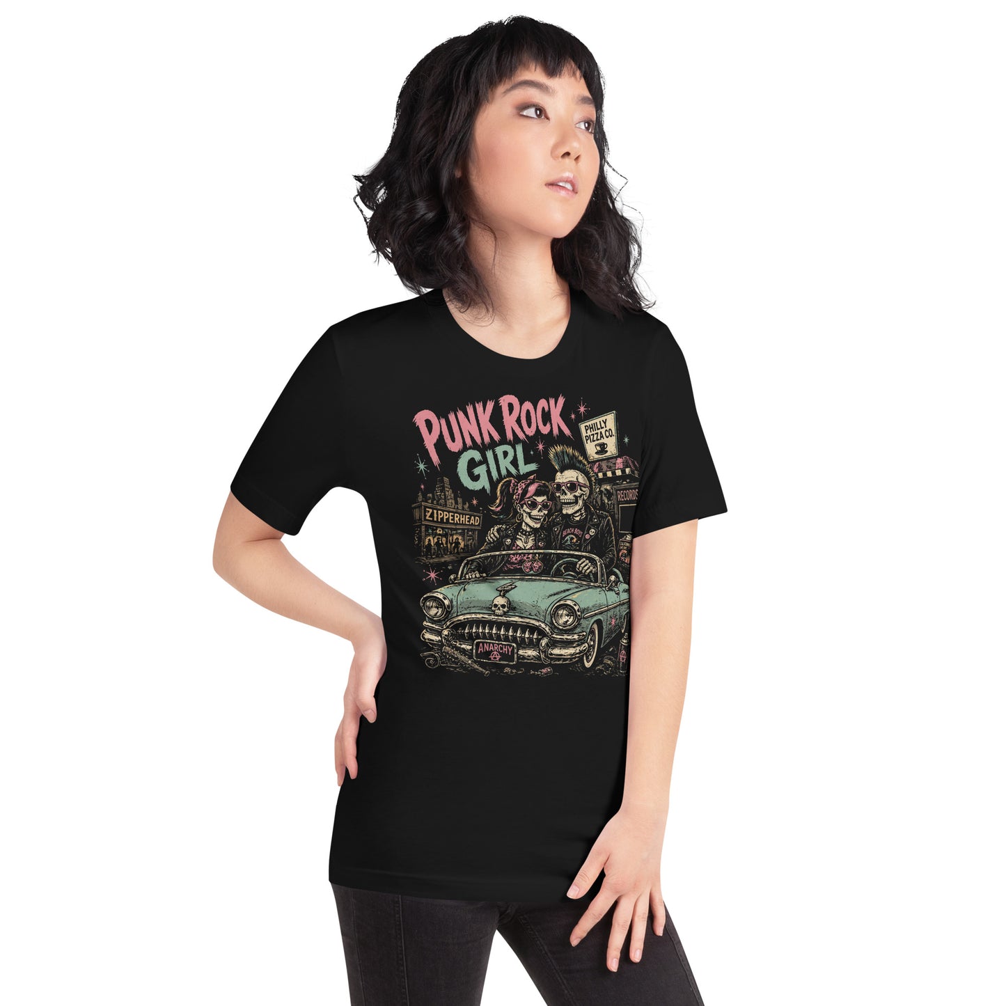 A retro-style graphic on a black t-shirt featuring two skeletons—a male with a mohawk and a female with a pink bow—driving a teal 1955 Chevy past iconic Philadelphia punk landmarks.
