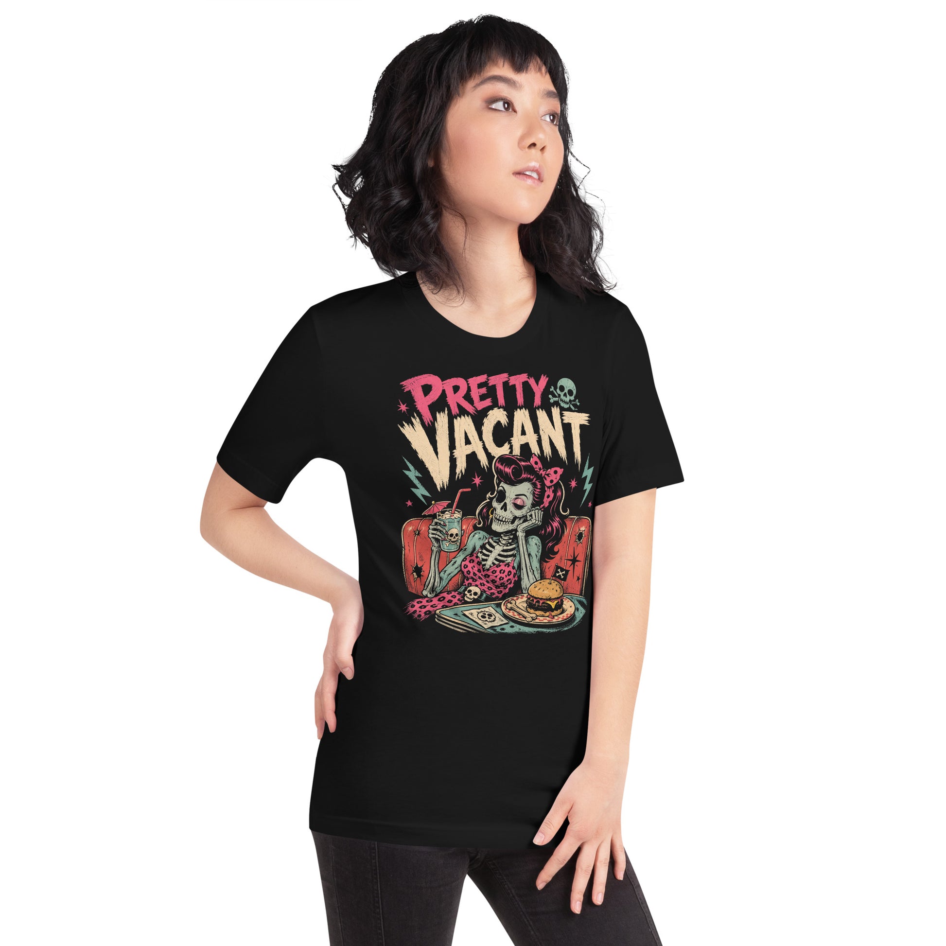 A retro-style graphic on a black t-shirt of a female skeleton pinup with pink hair in a diner booth, holding a skull-themed milkshake next to a burger with a crossbones flag.