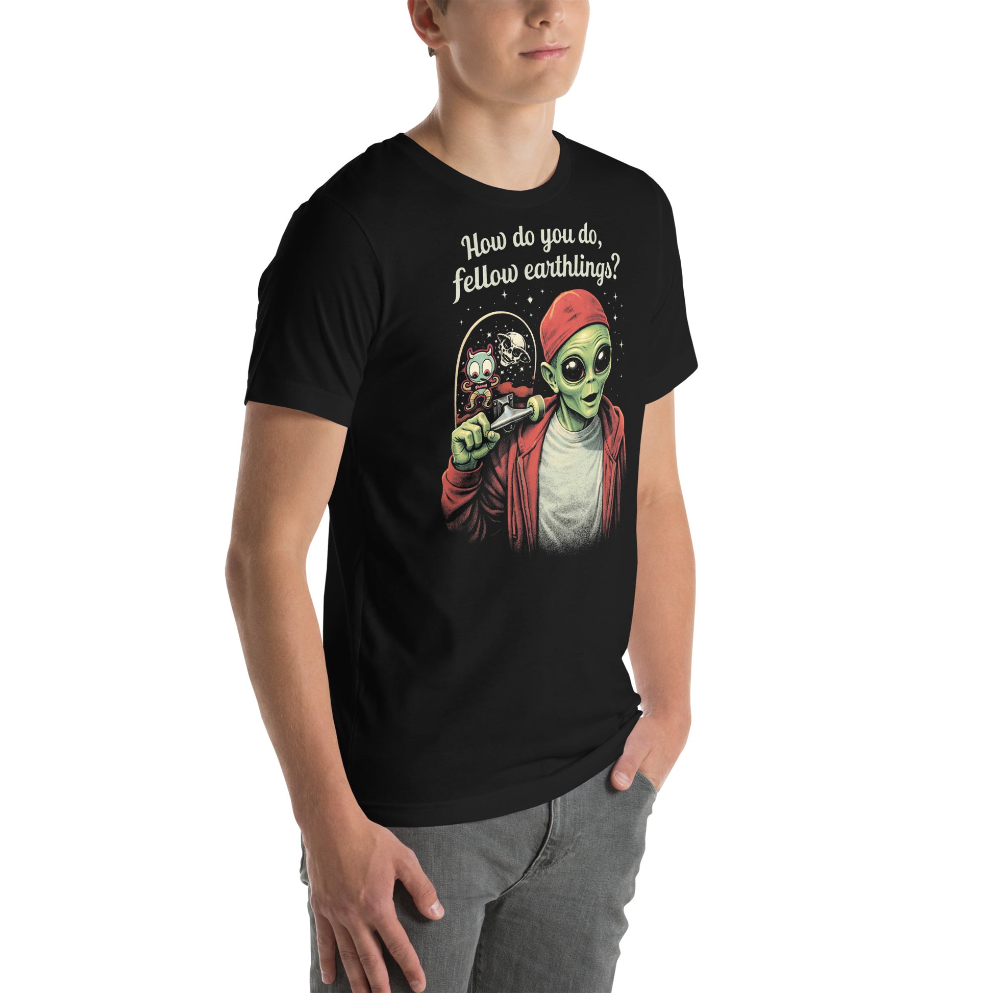 A retro-style graphic on a black t-shirt featuring a green alien on a skateboard, wearing a red hat and holding a skateboard, with the text "FELLOW EARTHLINGS.