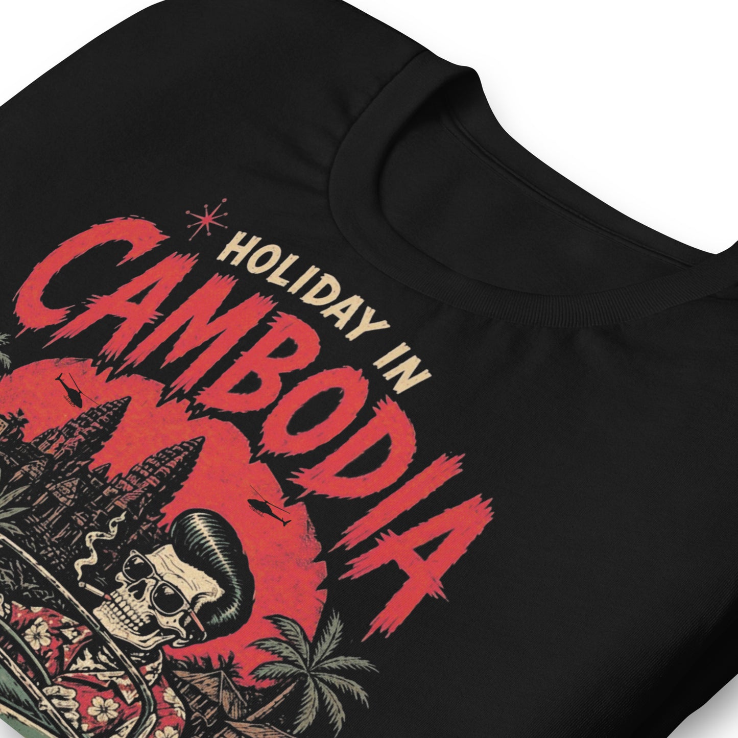 A detailed lowbrow graphic on a black t-shirt featuring a skeleton with a pompadour driving a 1955 Chevy convertible. The background shows Angkor Wat under a red sun with helicopters, and a sign that reads 'Paradise is Rotten'.