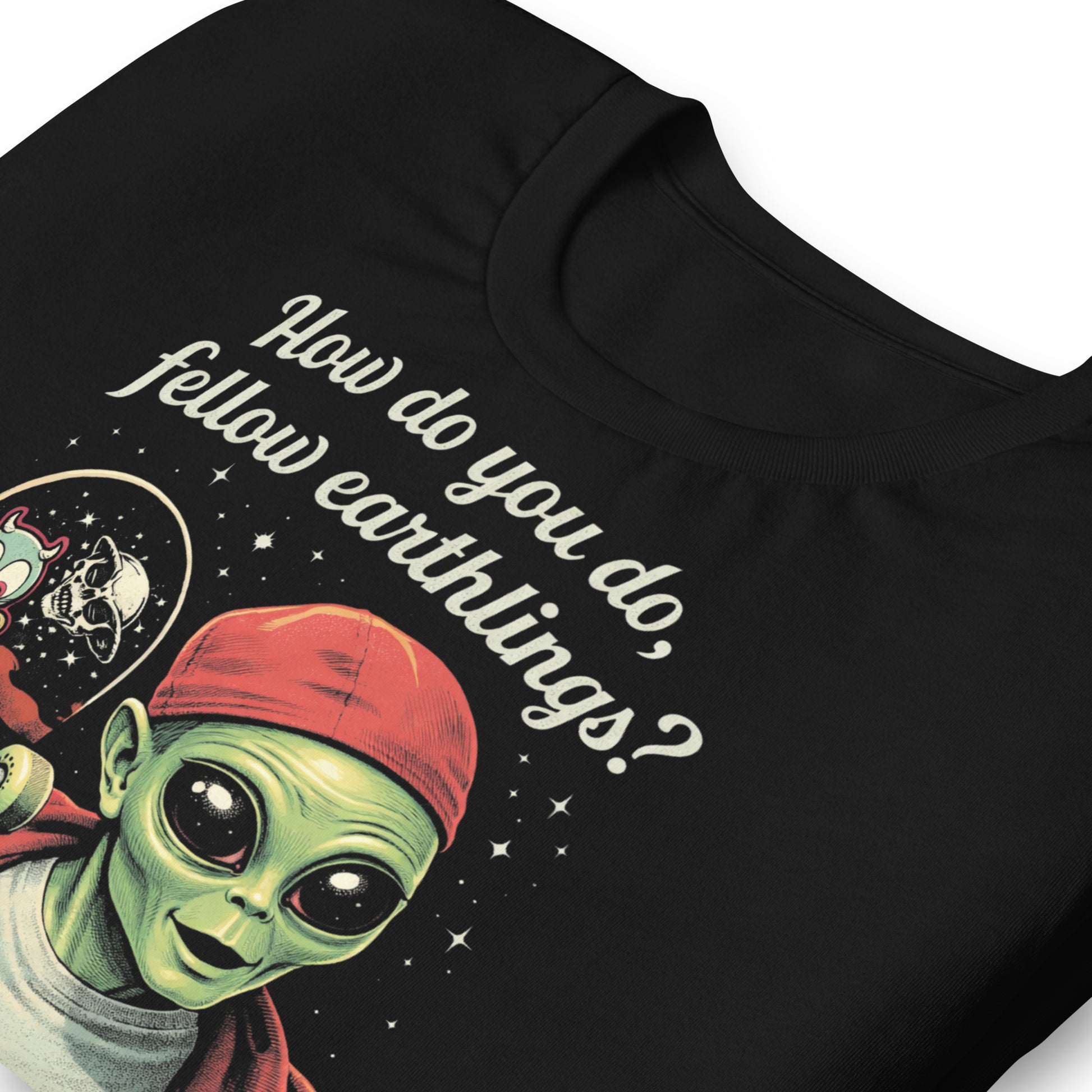 A retro-style graphic on a black t-shirt featuring a green alien on a skateboard, wearing a red hat and holding a skateboard, with the text "FELLOW EARTHLINGS.