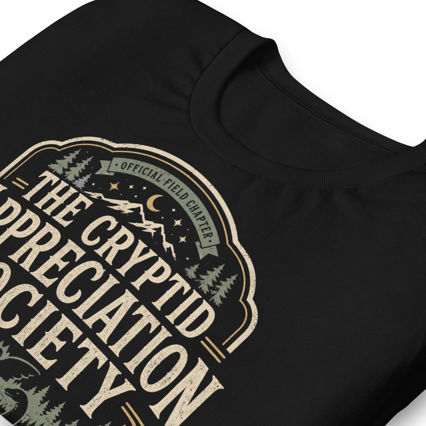 Black graphic tee featuring original Cinderpoint Studios artwork for The Cryptid Appreciation Society, a retro cryptid badge design with Sasquatch, Mothman, a Nessie-style lake creature, forest, mountains, moon, stars, and We Believe text.