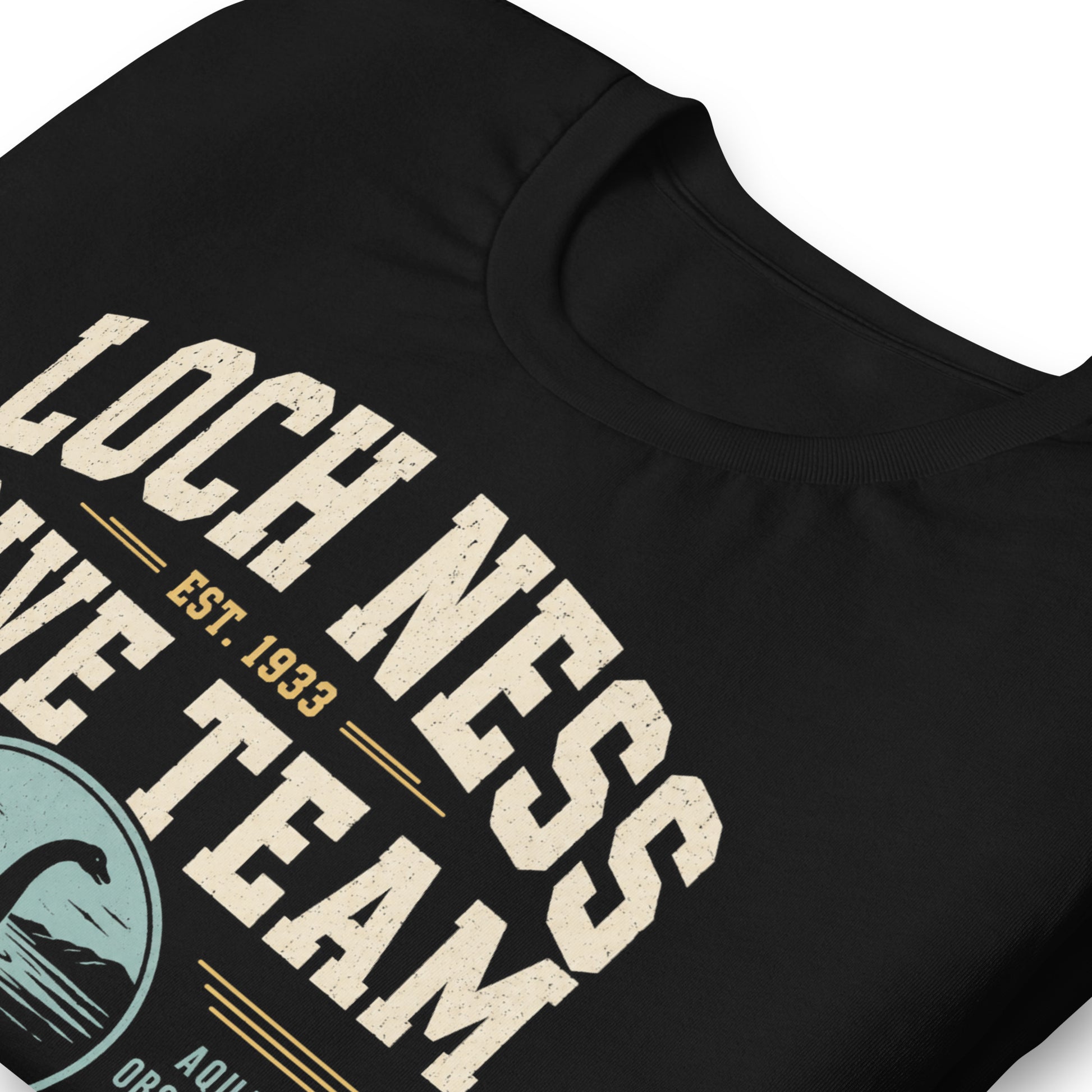 Black graphic tee featuring original Cinderpoint Studios artwork for Loch Ness Dive Team, a retro cryptid design with bold varsity lettering, a Nessie-style lake monster, diver, water scene, and text including Deep Water Division, Aquatic Observation Unit, We Believe, and Scotland Chapter.