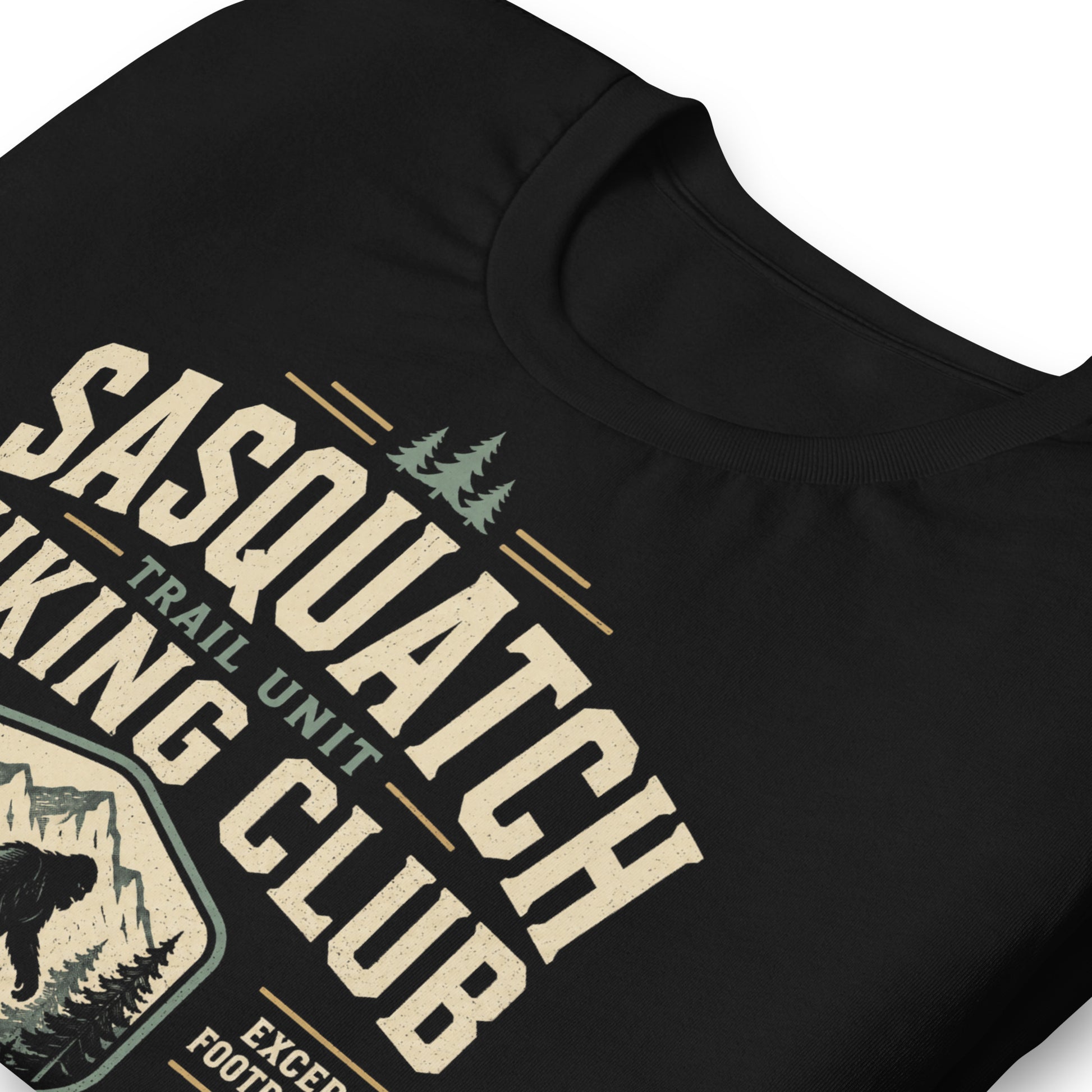 Close-up of the Sasquatch Hiking Club original Cinderpoint Studios artwork printed on a black tee, showing distressed retro lettering, Sasquatch silhouette, mountain scenery, pine trees, footprints, and Official Forest Division details.