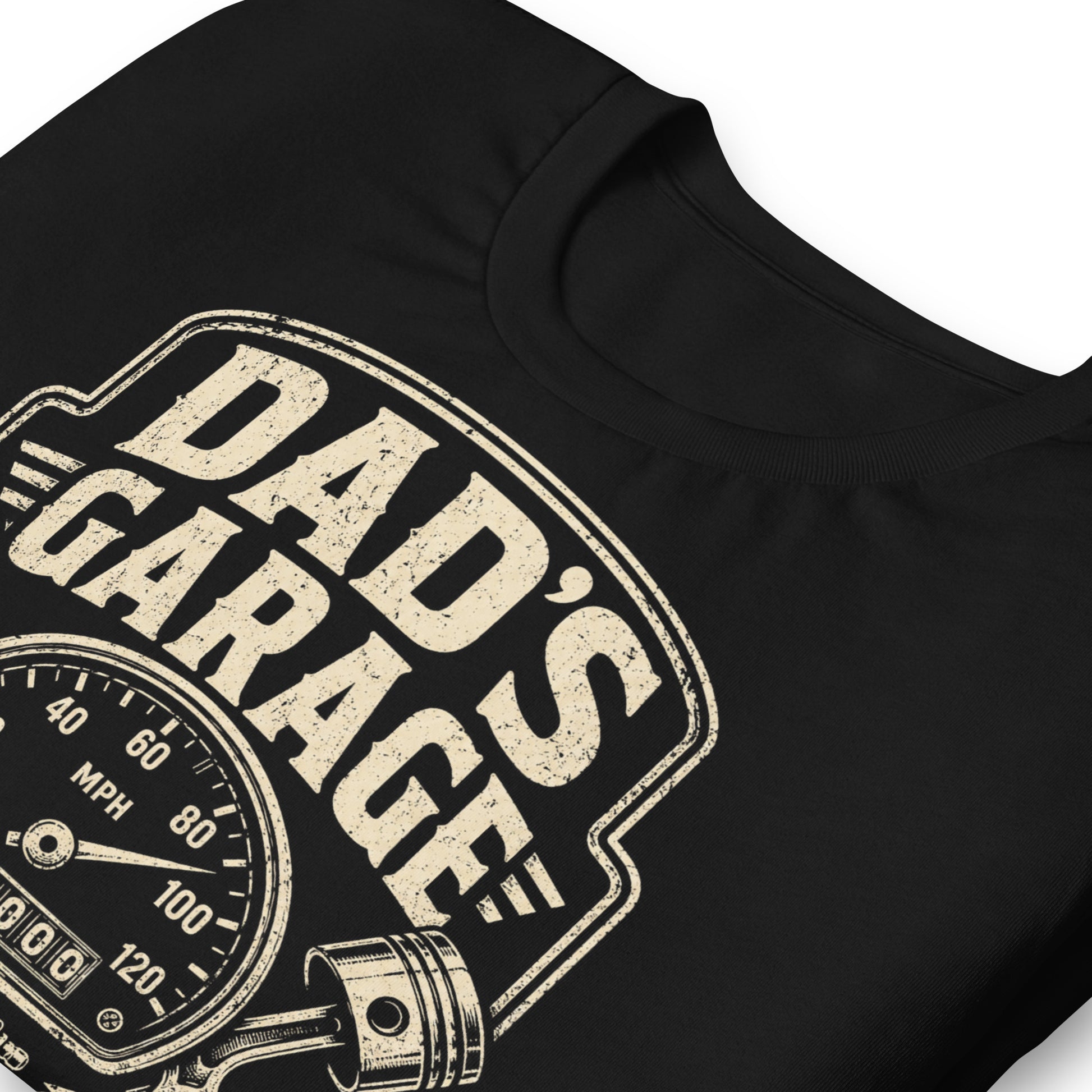 A black graphic tee featuring original Cinderpoint Studios artwork for Dad’s Garage, a one-color retro garage badge design with bold lettering, a speedometer, pistons, spark plug, wrench, and High Mileage Low Tolerance text.