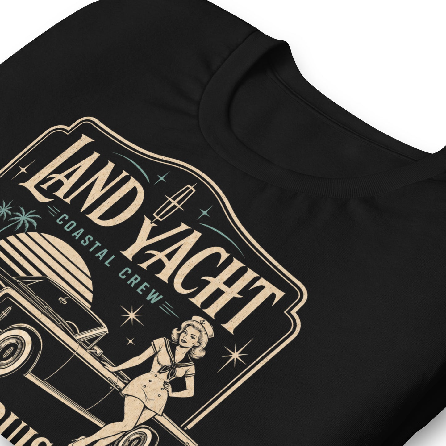 A black graphic tee featuring original Cinderpoint Studios artwork for Land Yacht Luxury Cruisers, a retro classic car design with a 1960s luxury convertible inspired by the 1965 Continental, a sailor pinup, atomic accents, palm trees, and bold vintage lettering.