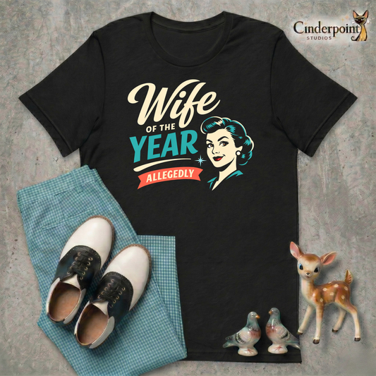 A top-down flat-lay on a grey concrete surface featuring the 'Wife of the Year Allegedly' black tee. Included are teal gingham pants, black and white saddle shoes, and vintage ceramic figurines.